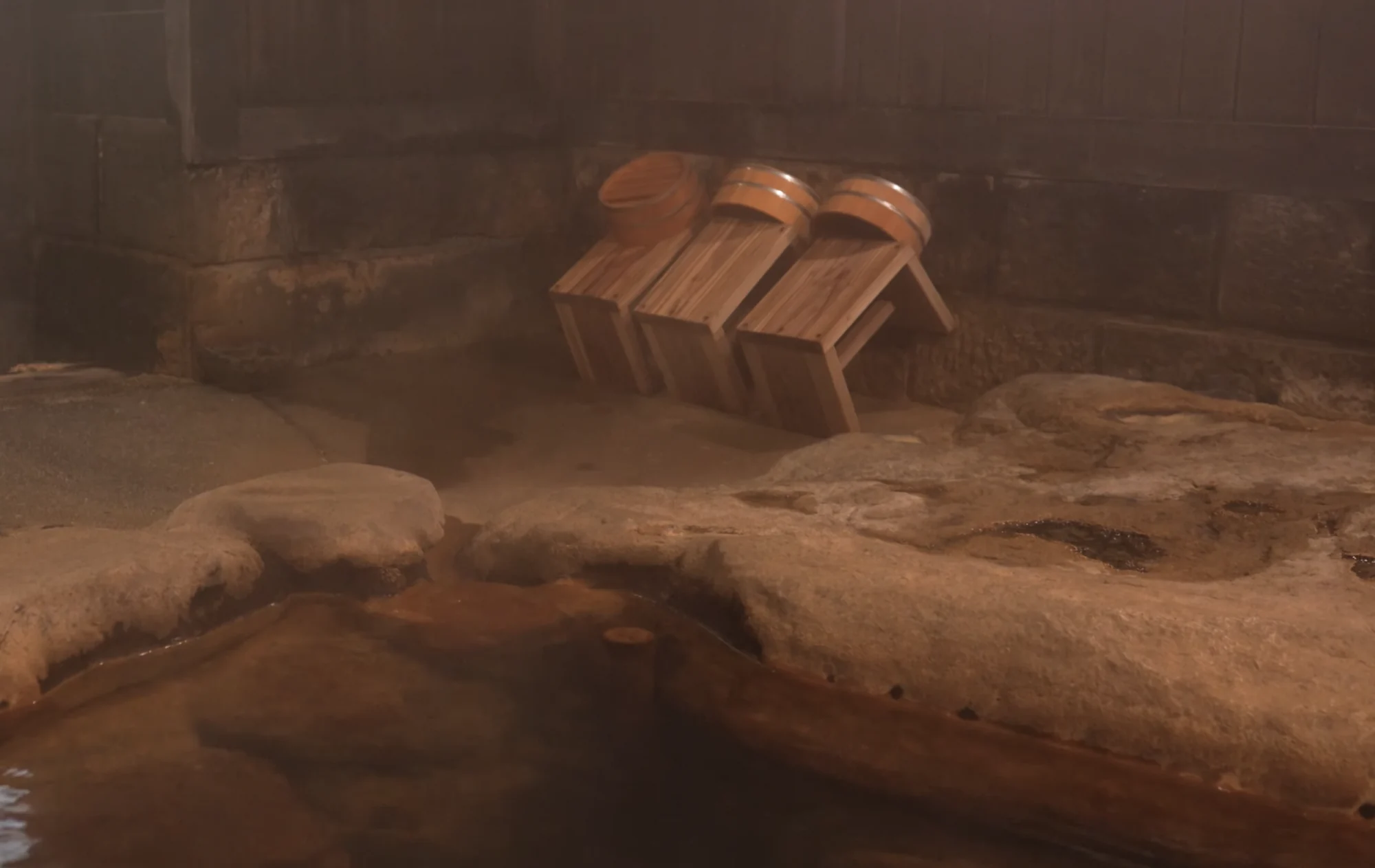 Wooden onsen buckets and low stools stacked at a bath edge in steam