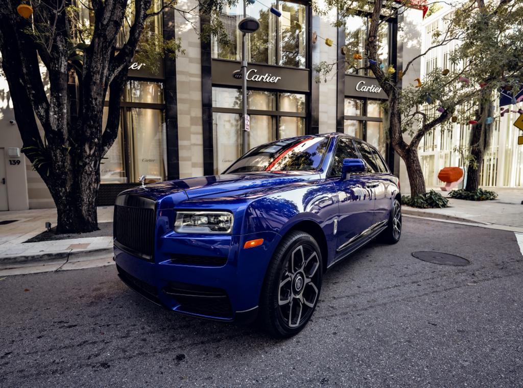 Rolls-Royce Cullinan luxury SUV in metallic blue finish parked on cobblestone street, front quarter view showing iconic grille and Spirit of Ecstasy hood ornament