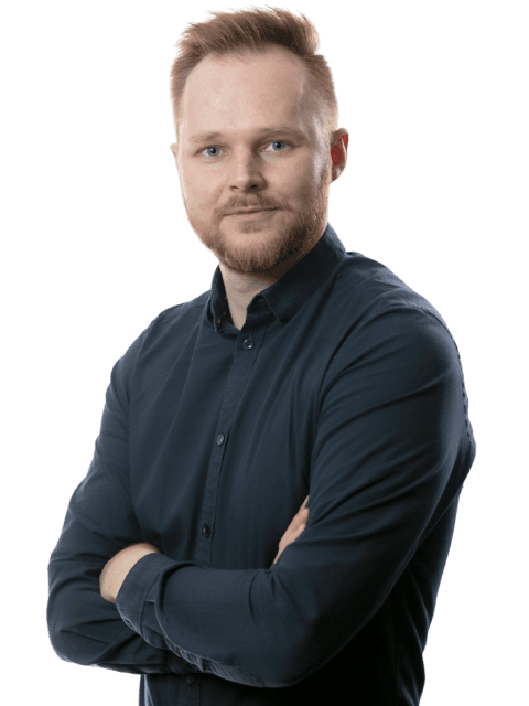 A confident person with short hair, wearing a dark sweater, stands with arms crossed, looking directly at the camera.