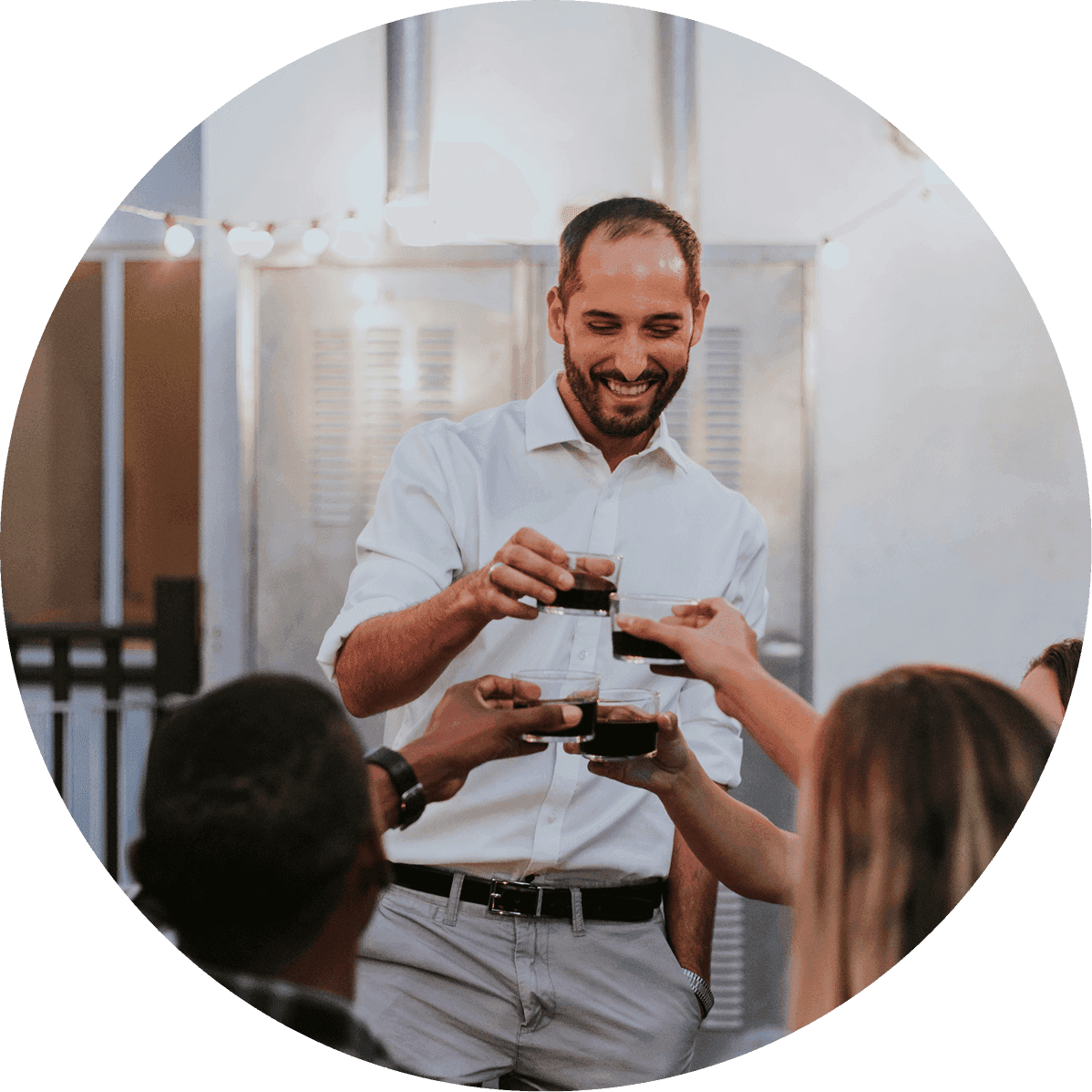 Man smiles while raising a glass with a group gathered around him