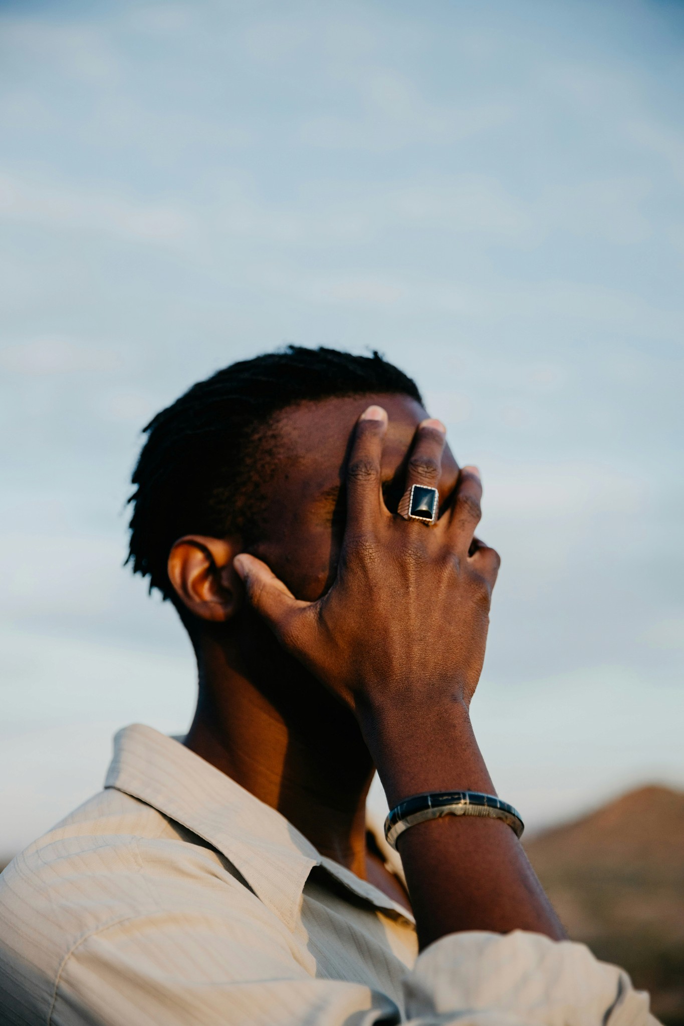 Man covering face with hand, wearing a ring.