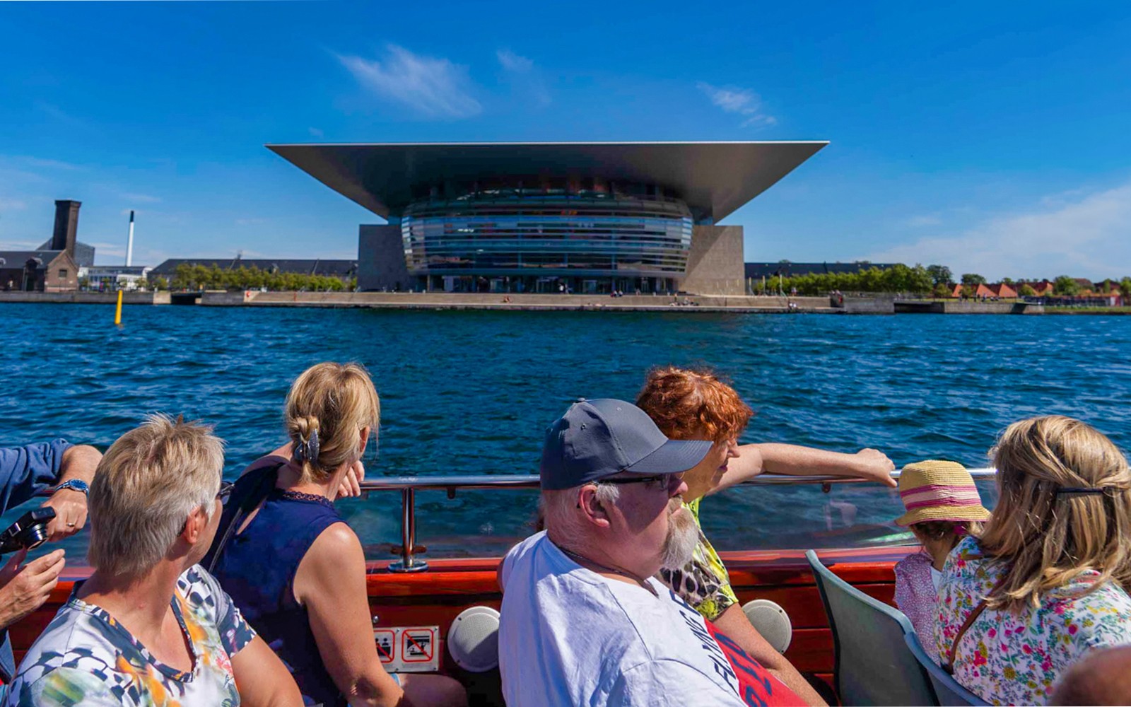 Turisták egy hajón, amint a Koppenhágai Operaházat nézik egy csatornahajózás során.