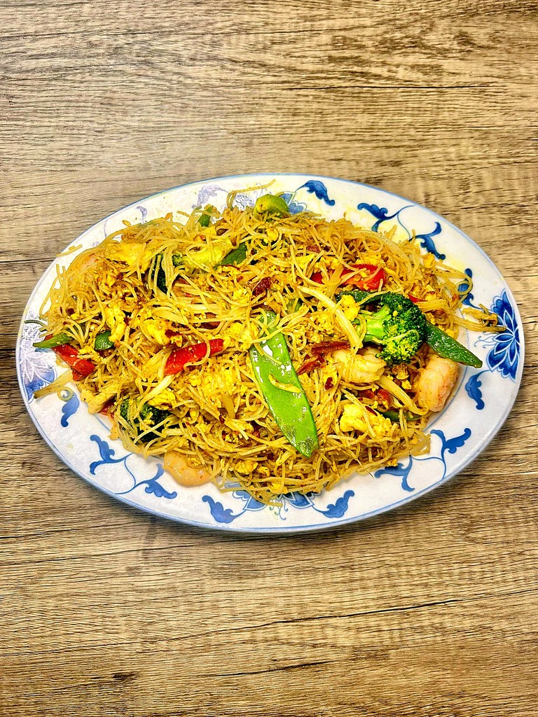 Thin rice noodles tossed with shrimp, peppers and snow peas on a blue-and-white platter