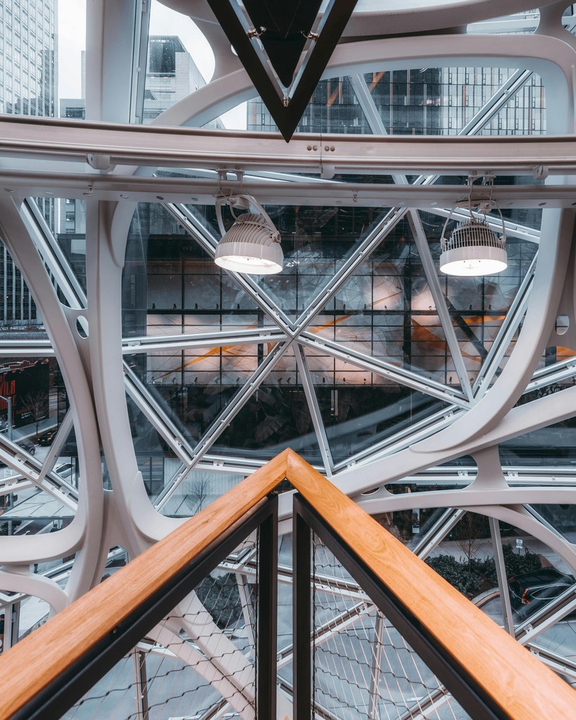 An image of a striking modern architectural structure with geometric patterns and glass panels, viewed from a balcony railing, likely representing an innovative or futuristic building design.