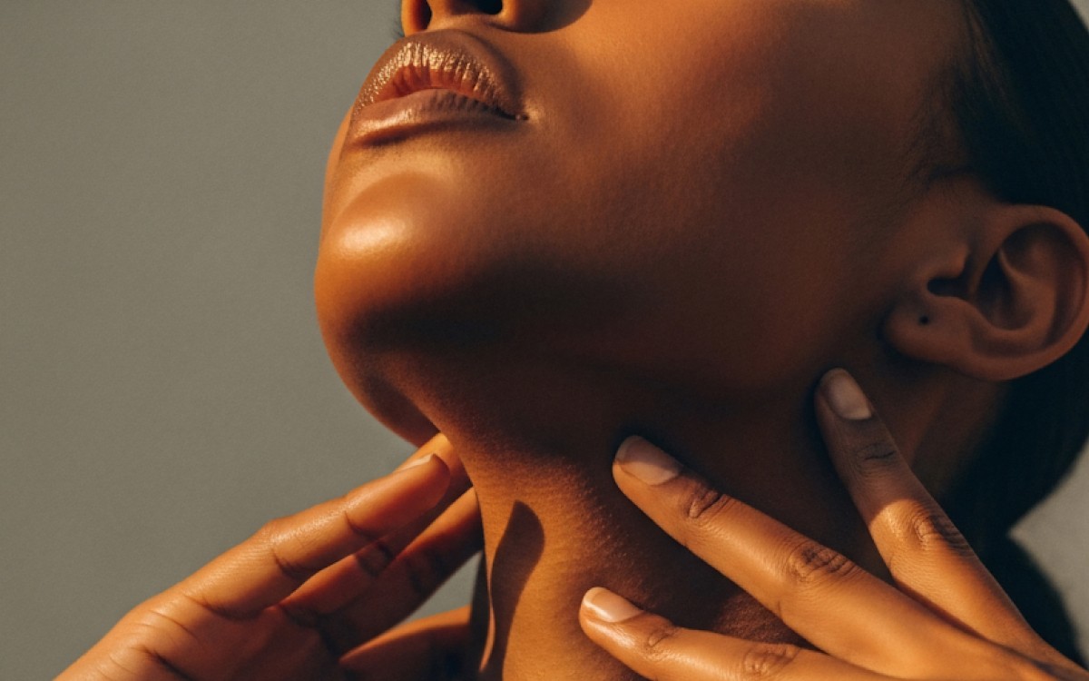 Close-up of a woman's neck and lips, bathed in warm light. Hands gently touch her neck, conveying relaxation and tranquility.