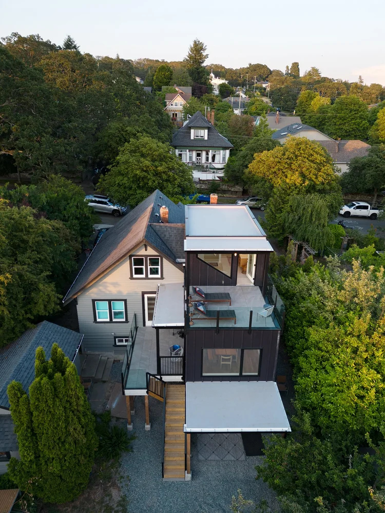 Modern two-story home with large glass windows, warmly lit interiors, and a balcony. Surrounded by trees and a manicured lawn at dusk. Cozy ambiance.