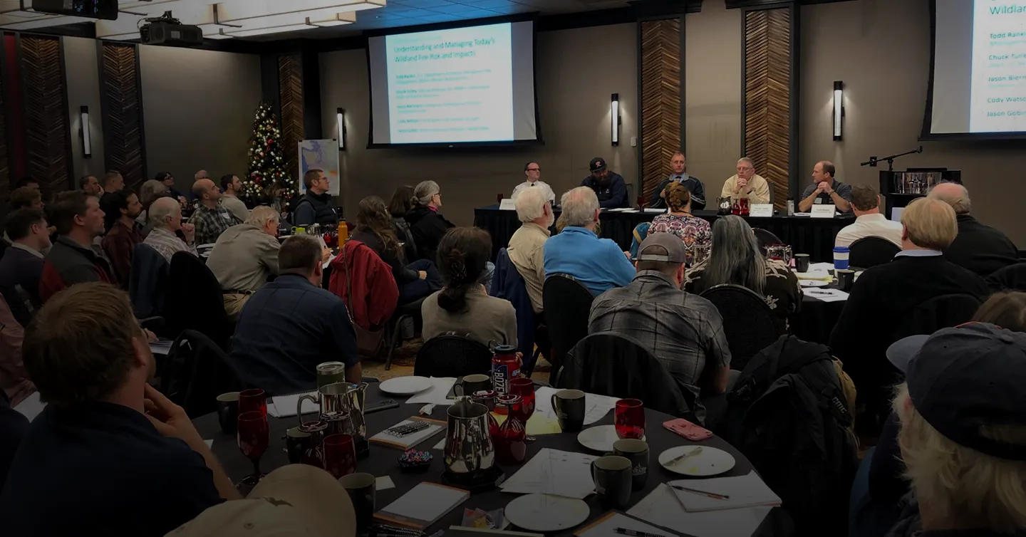 A convening of Puget Sound climate and planning practitioners with a panel in the back facing the viewer, slides behind them, and an audience in the foreground facing the panel.