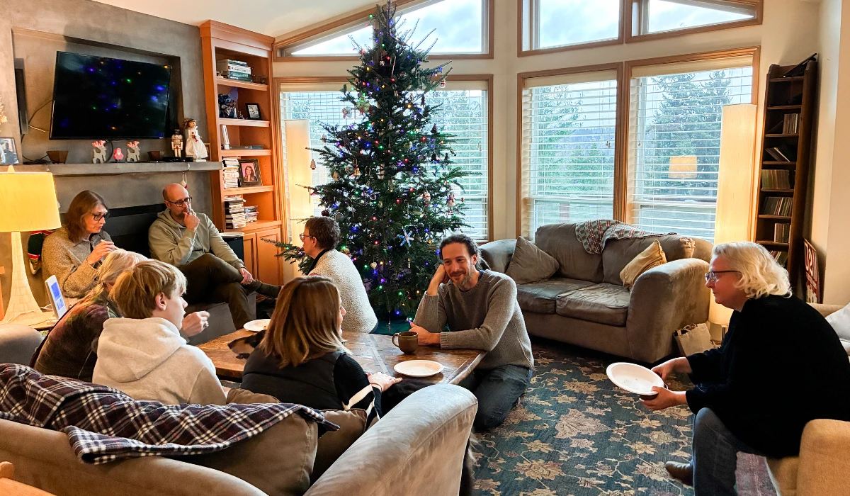 Community members gathered in a living room, sitting together and sharing conversation during a winter holiday gathering.