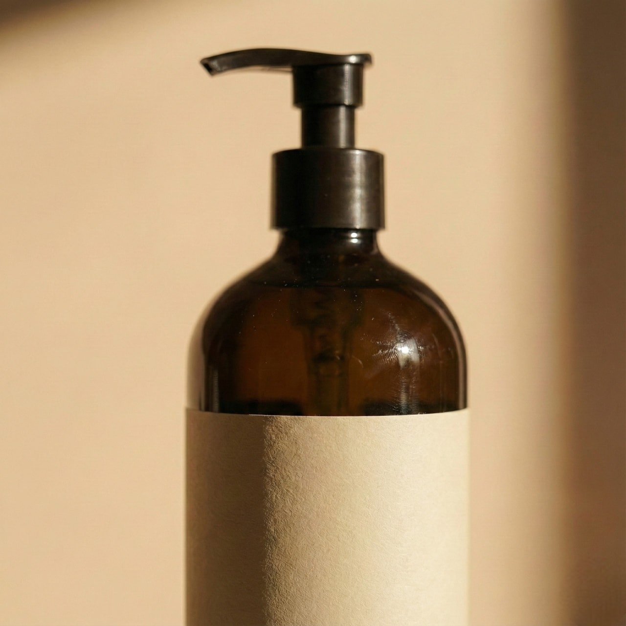 Brown glass pump bottle with a blank beige label, set against a soft, neutral background. The lighting creates a warm, minimalist ambiance.