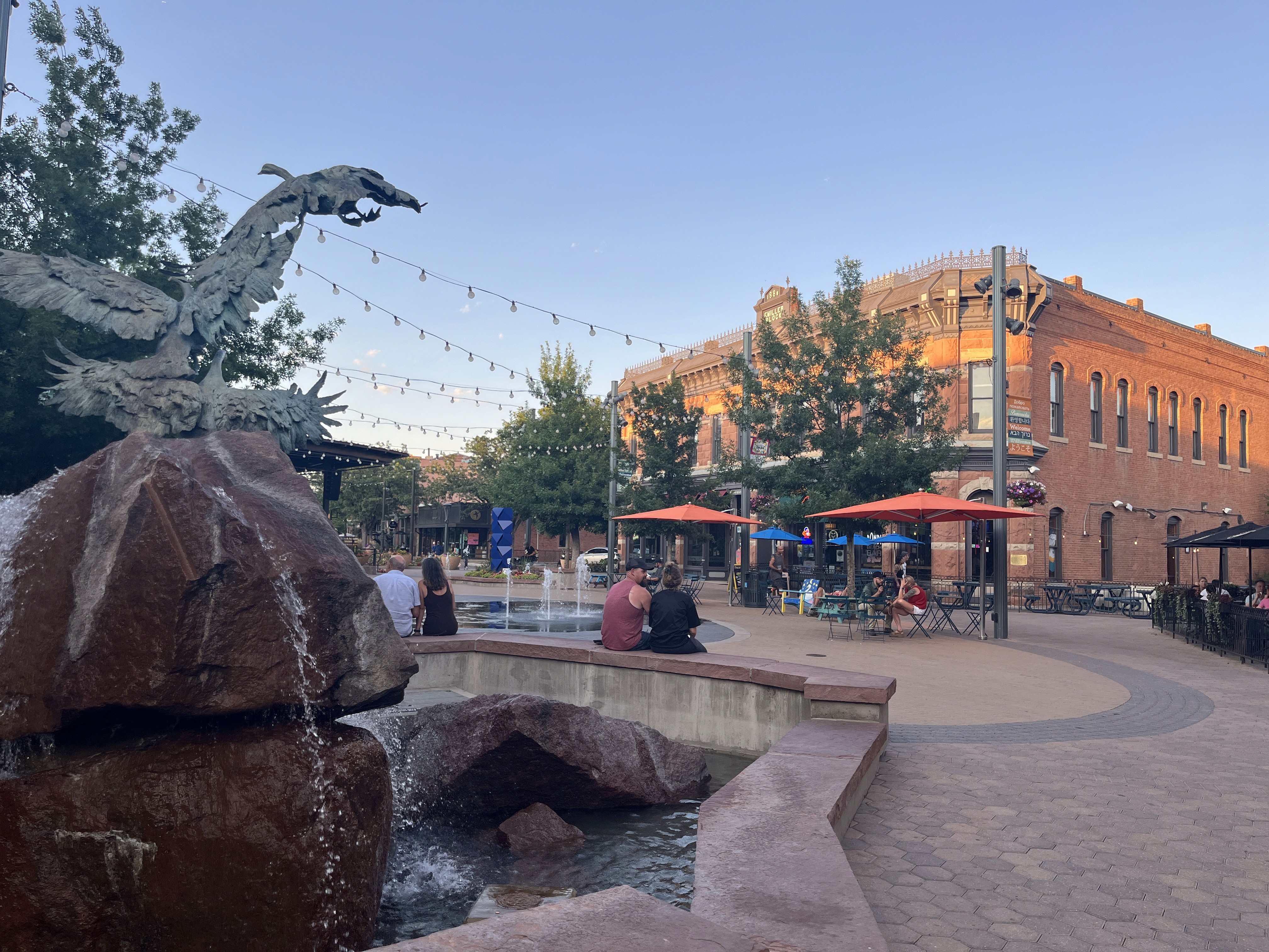 Fort Collins Old Town Square at sunset with fountain and brick buildings.