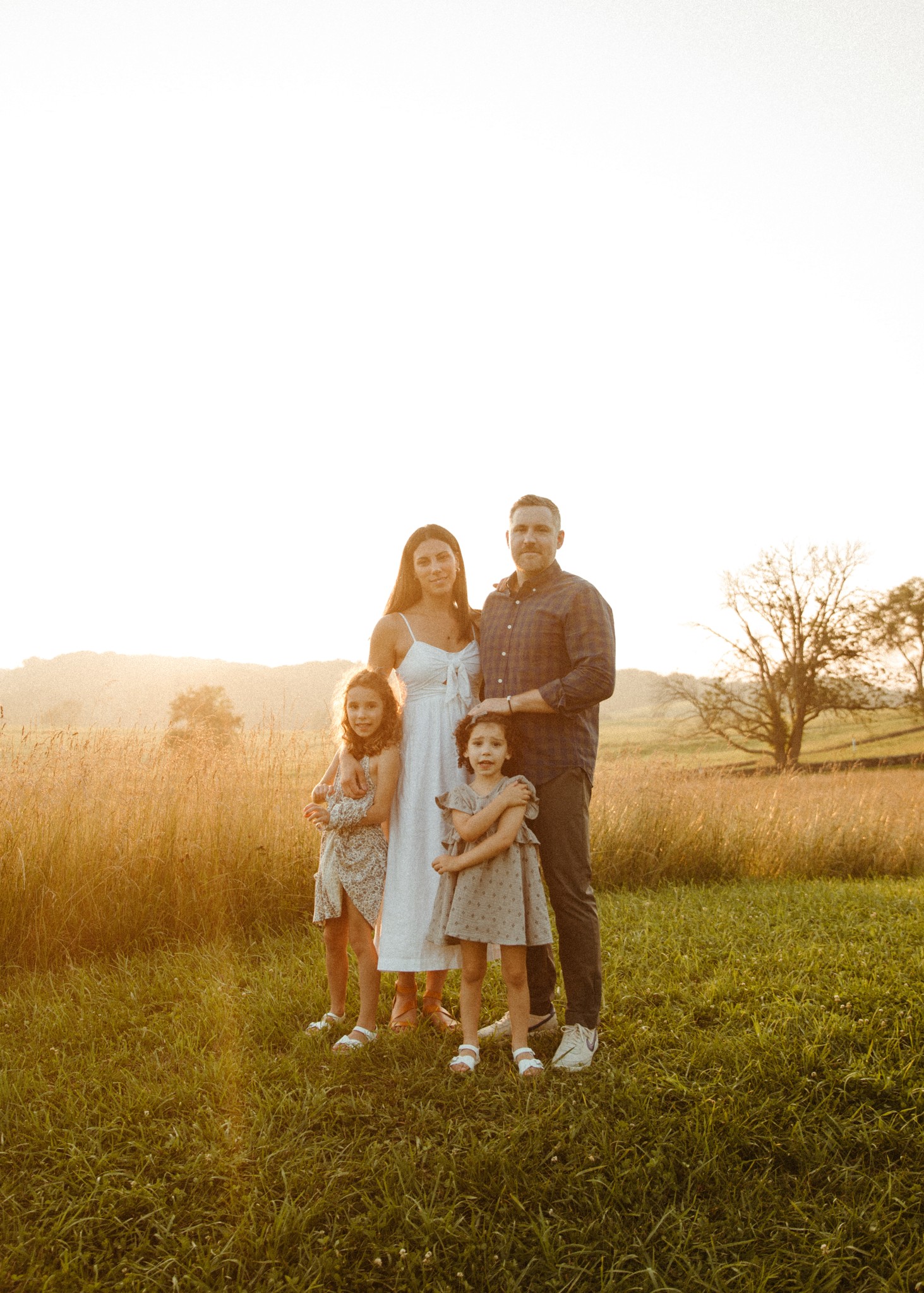A side-profile of a young person with dark, wavy hair, wearing silver sports sunglasses and a black sweater, sitting in front of a blurred teal couch.