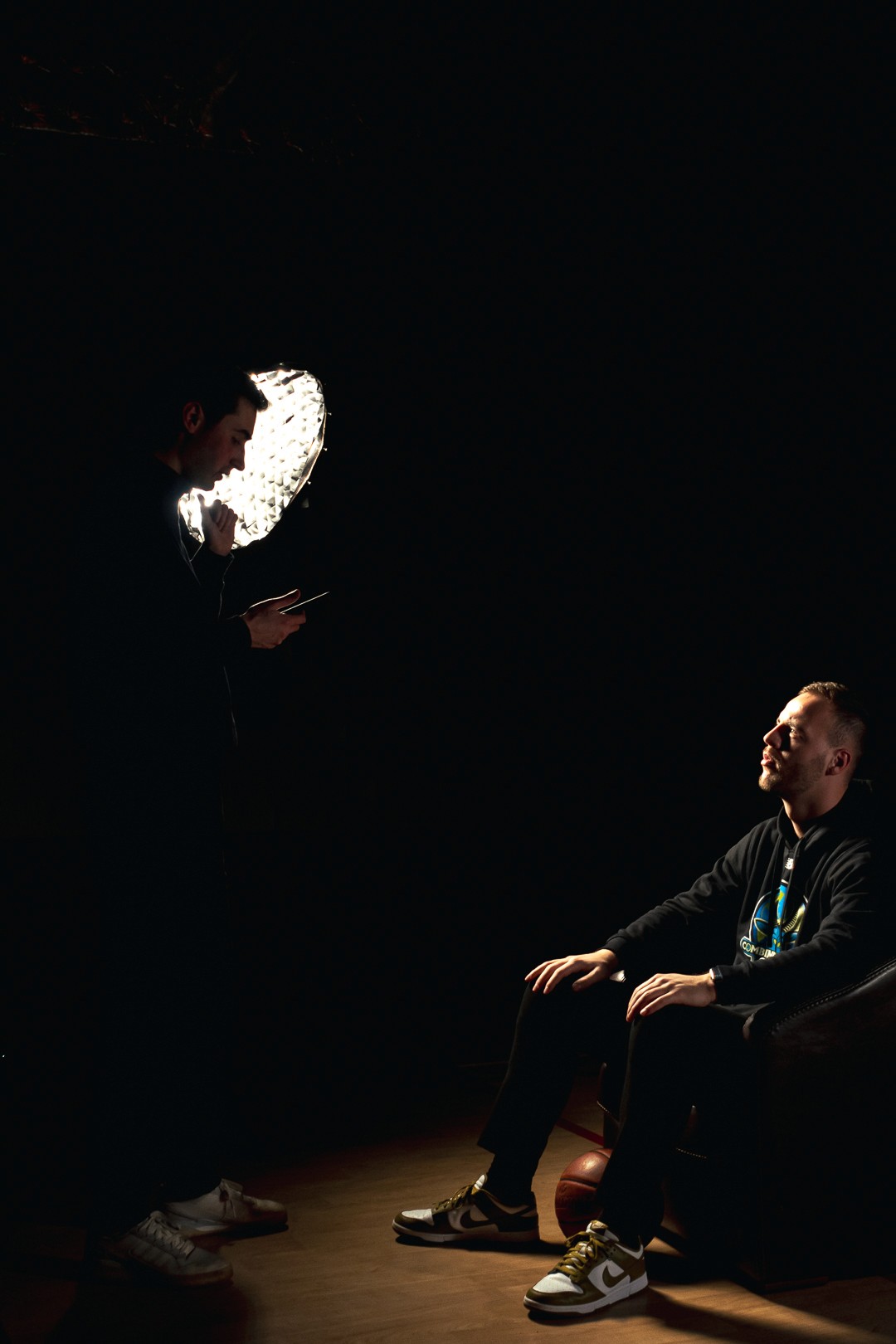 Homme assis sous une lumière de studio, un réalisateur lui donnant des instructions