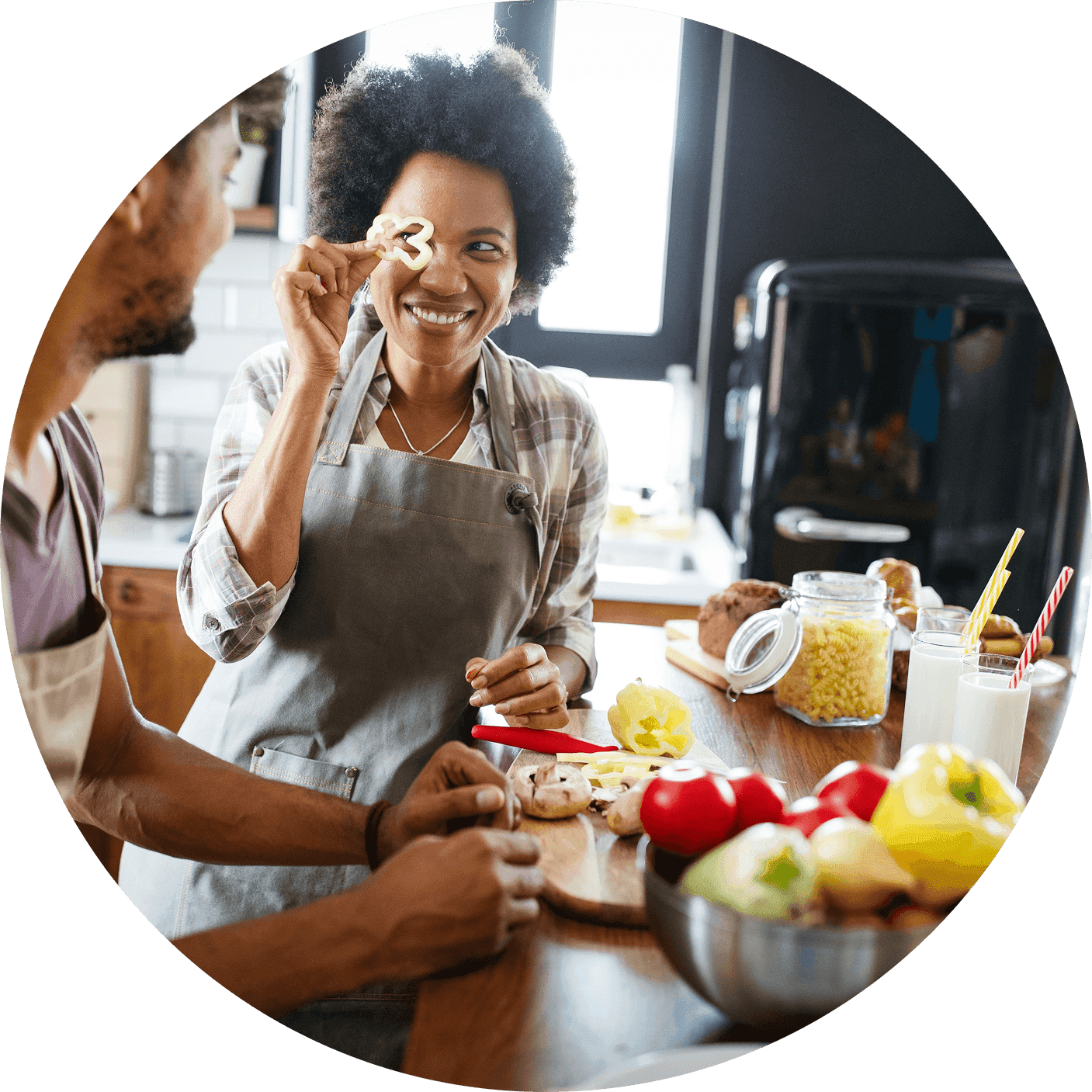Woman in an apron smiles while holding up a sliced mushroom as another person chops vegetables nearby