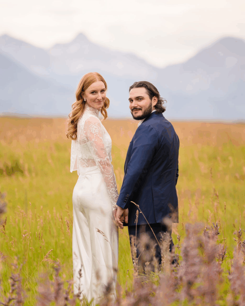 Newlyweds posing together in a meadow with mountains behind them