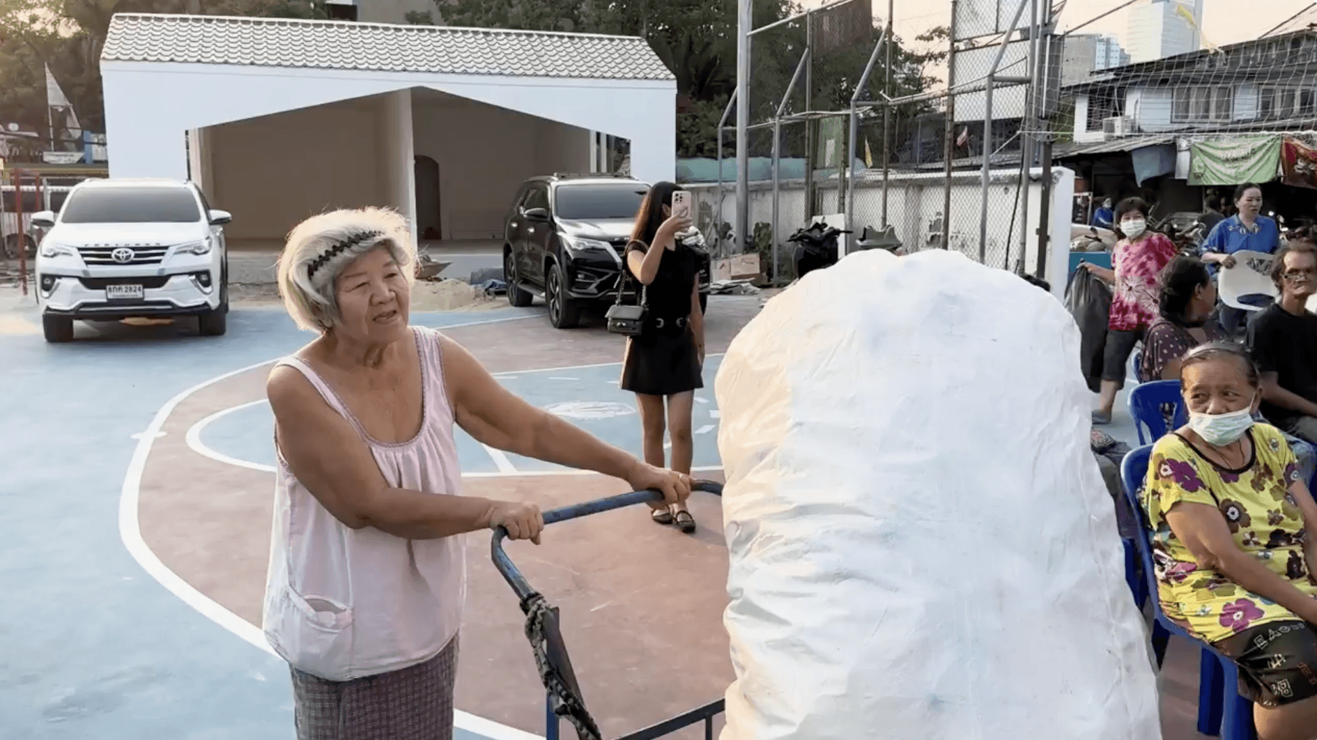 man in blue t-shirt and white floral skirt holding black smartphone while sitting on sidewalk