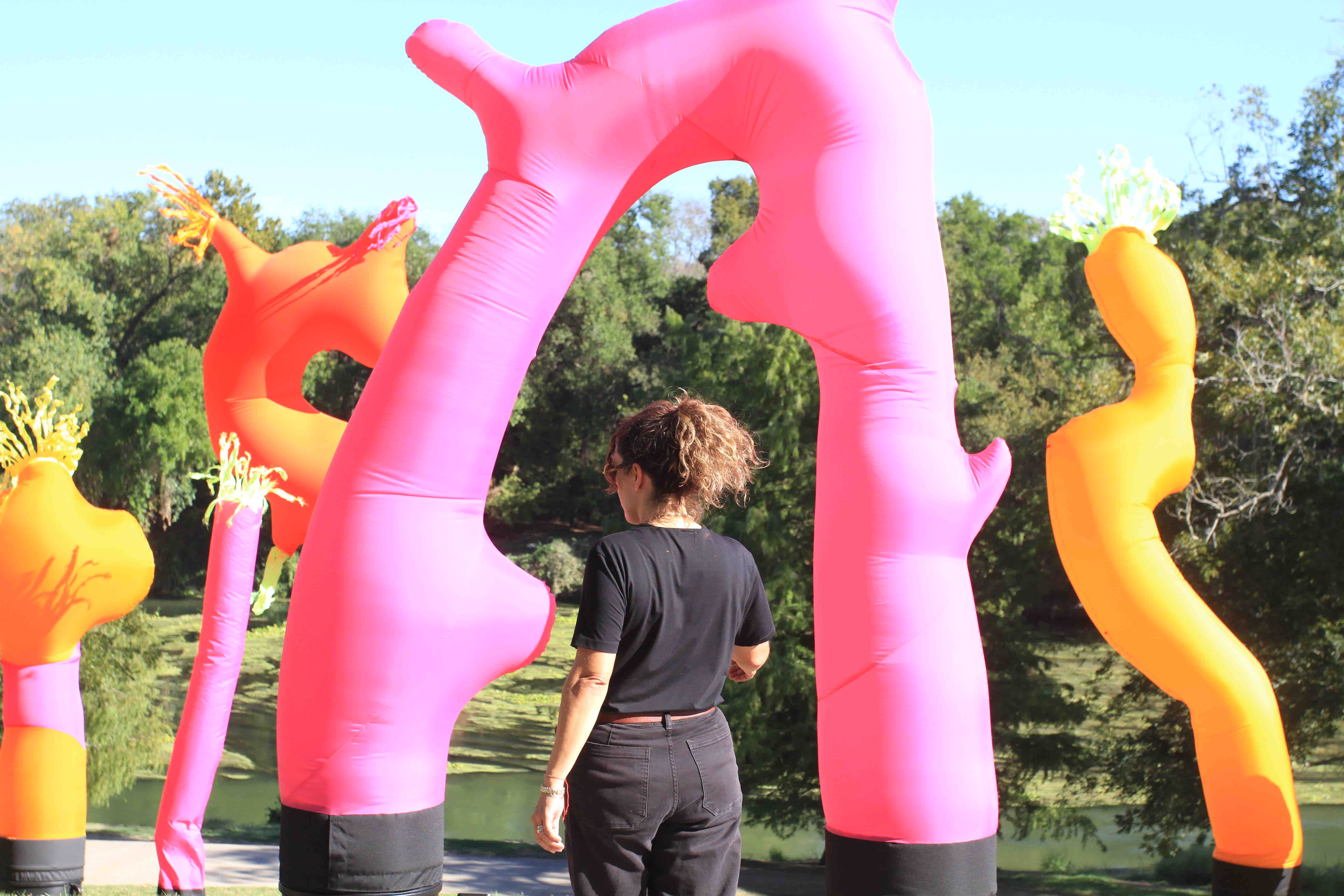 A person stands in front of colorful, twisted inflatable sculptures in a sunny outdoor setting.