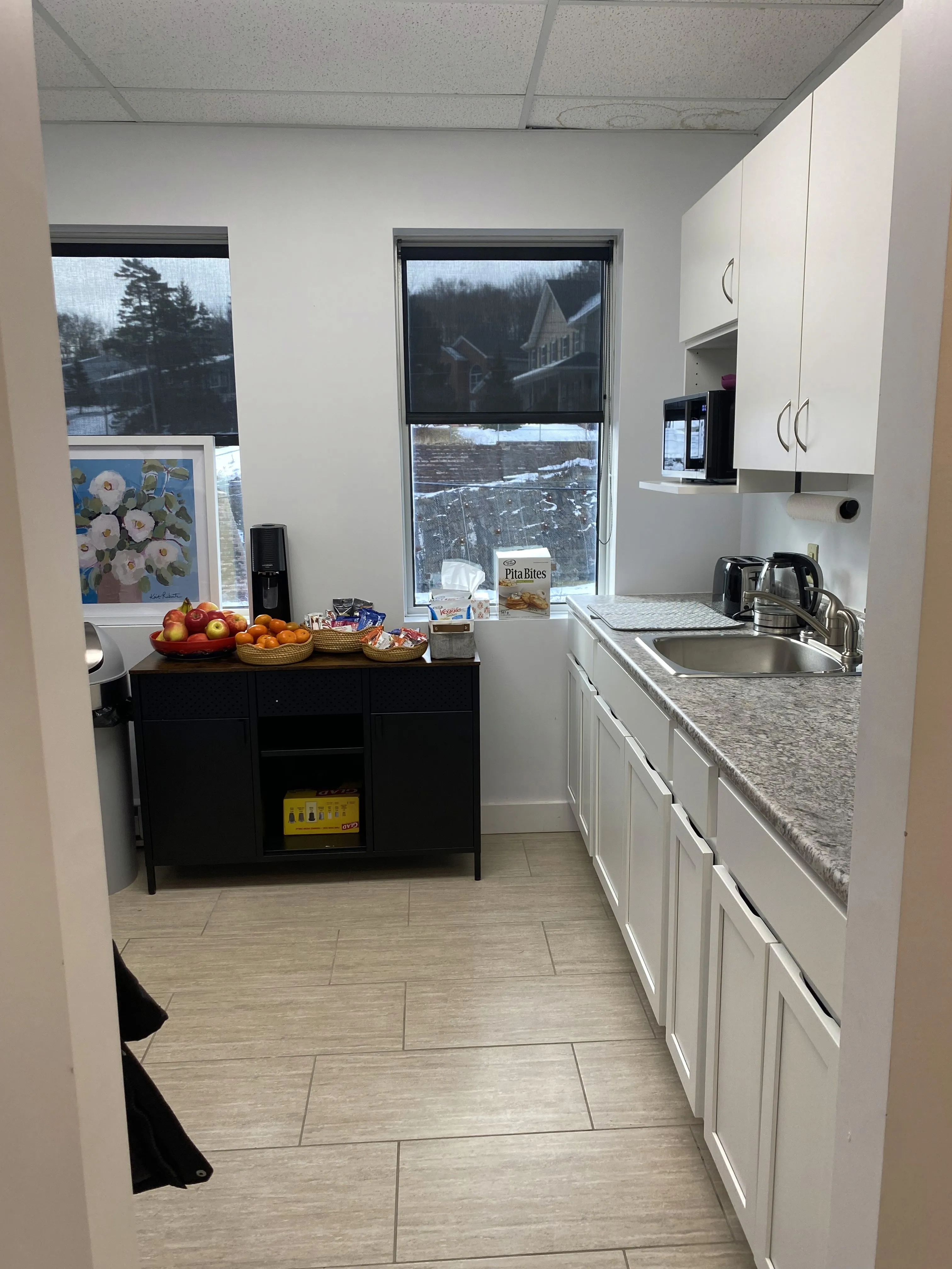 Break room kitchenette with a coffee maker, fruit baskets, snacks, and white cabinetry beside a sink