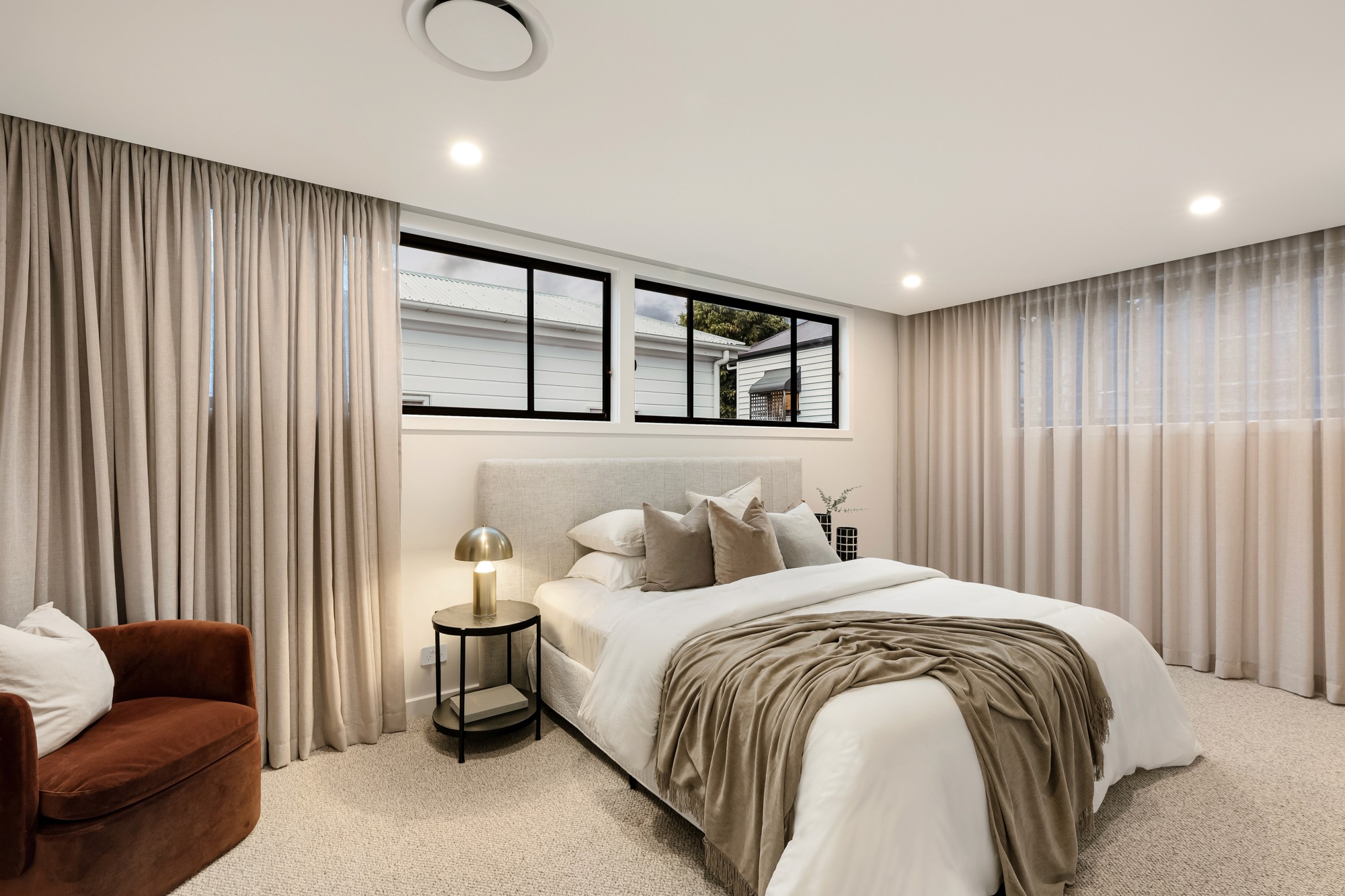 Bedroom with soft sheer curtains, neutral-toned bedding and warm lighting.
