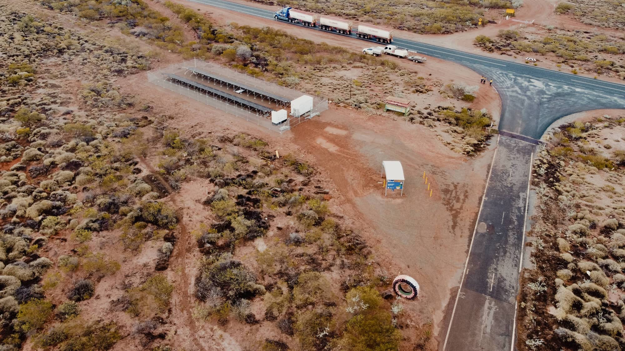 Aerial view of a remote solar power array under construction next to a highway in Australia, with trucks and vehicles nearby.