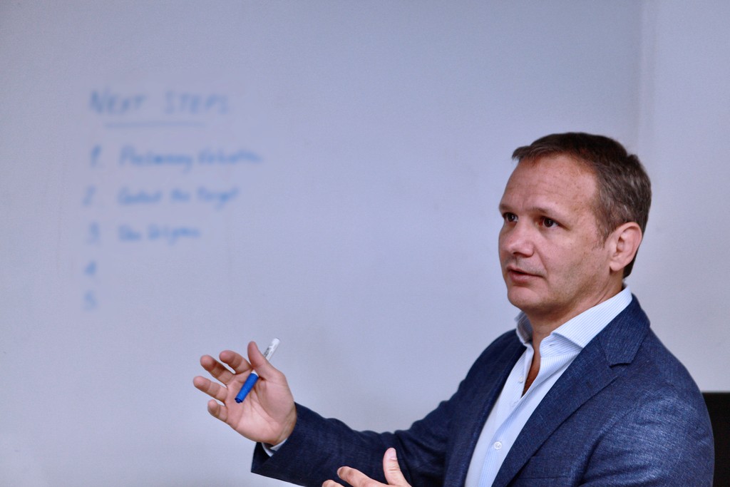 Smiling man wearing glasses and a pink shirt, showing his arm with a bandage after vaccination.