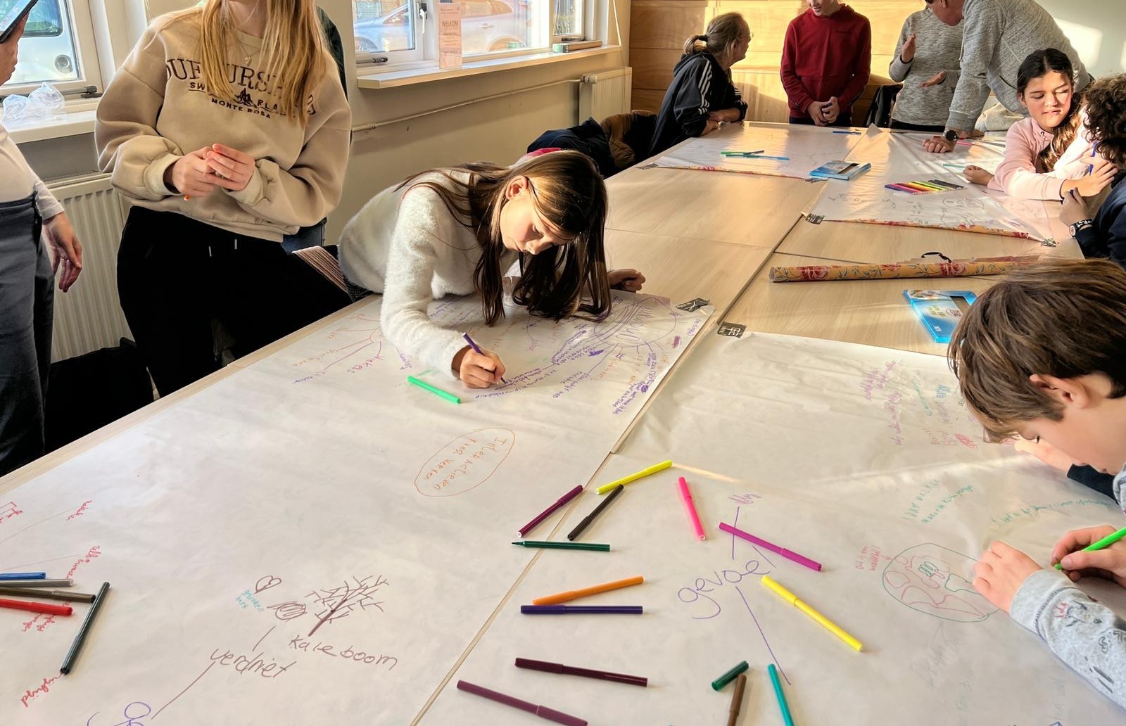 Kinderen werken aan een creatieve opdracht aan een grote tafel vol papier en stiften