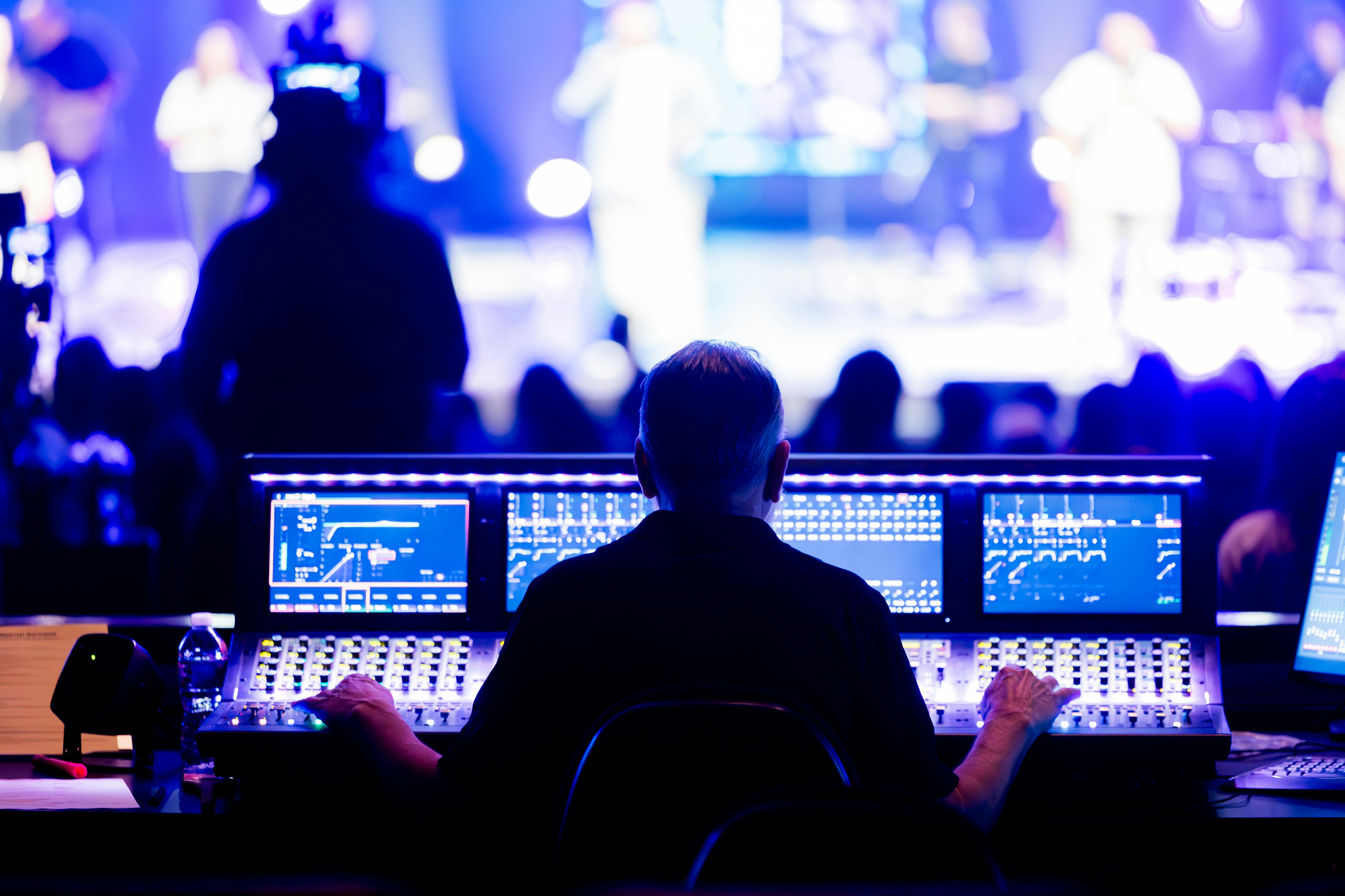 Audio engineer operating a digital sound mixing console during a live production, managing sound levels for performers on stage.