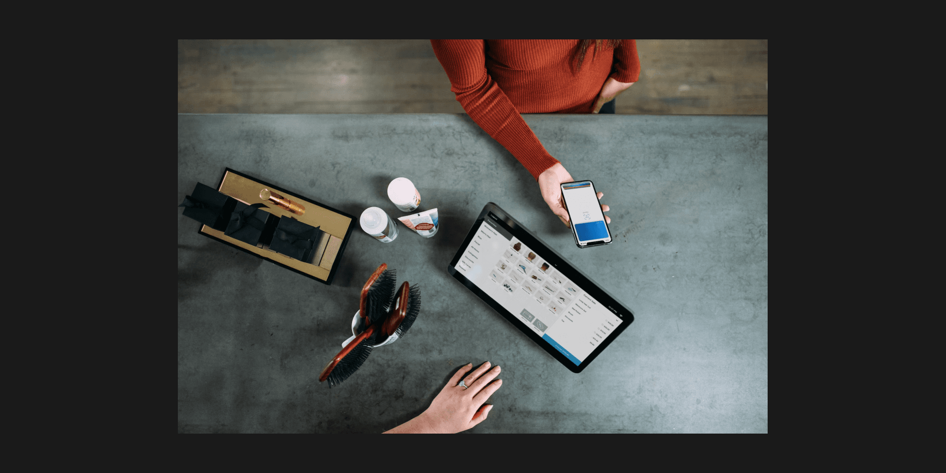 Overhead view of a point-of-sale transaction with a tablet, a smartphone, and two pairs of hands on a counter