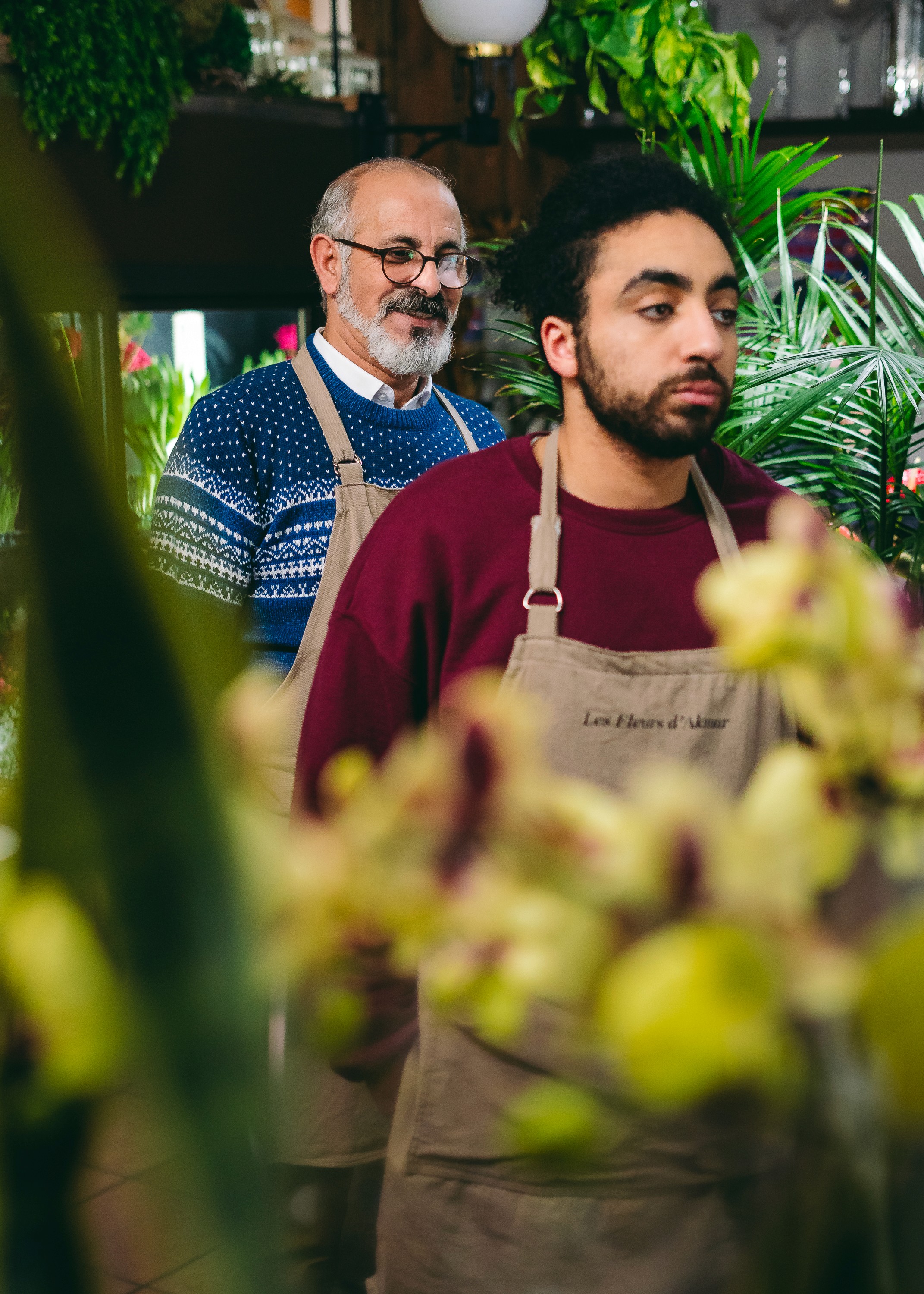 Anas Hassouna à l'air blasé avec son oncle souriant (Said Benyoucef) en arrière plandans leur boutique de fleuriste.
