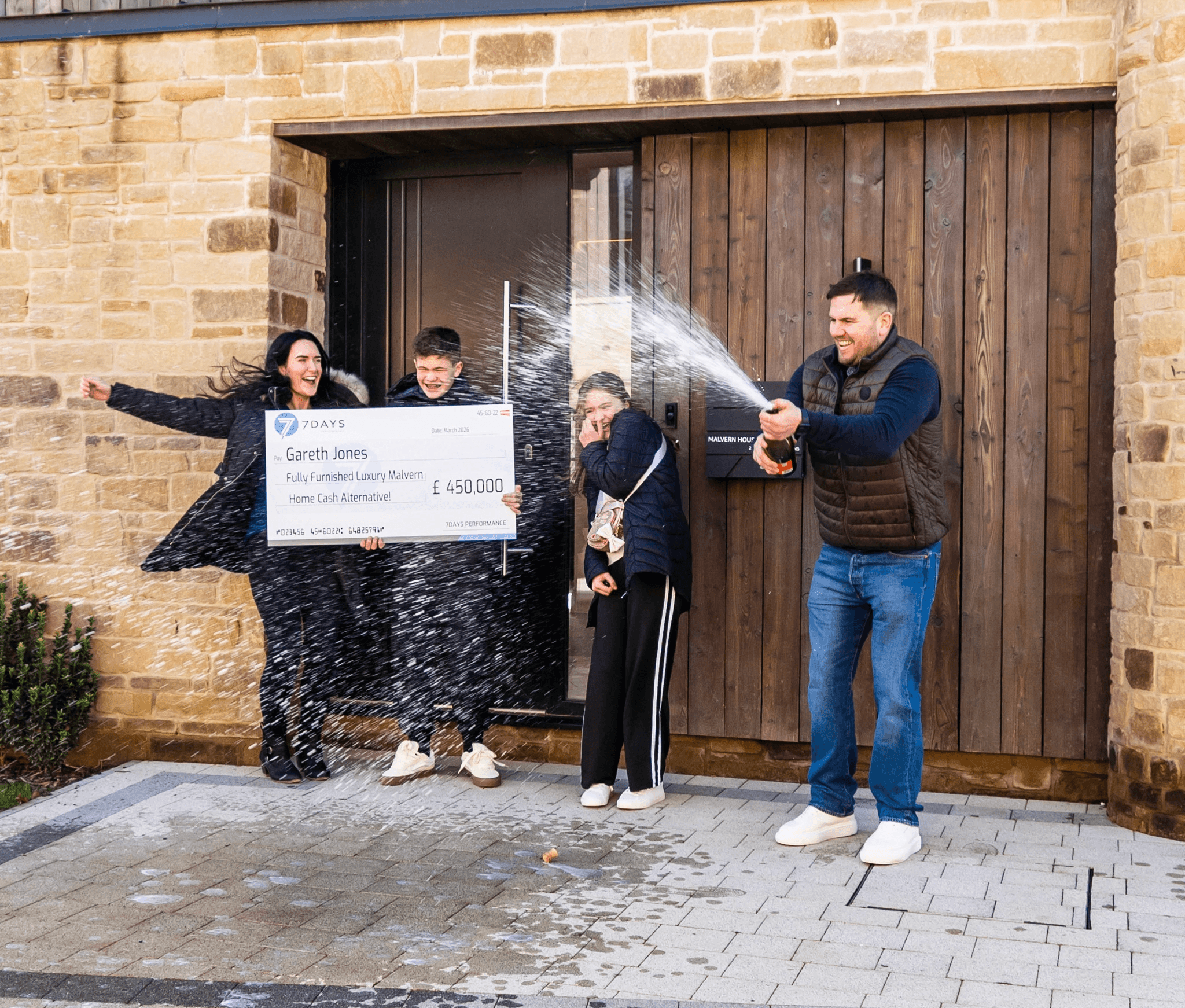 Family of four stand in a moden kitchen with an oversized cheque for £450,000