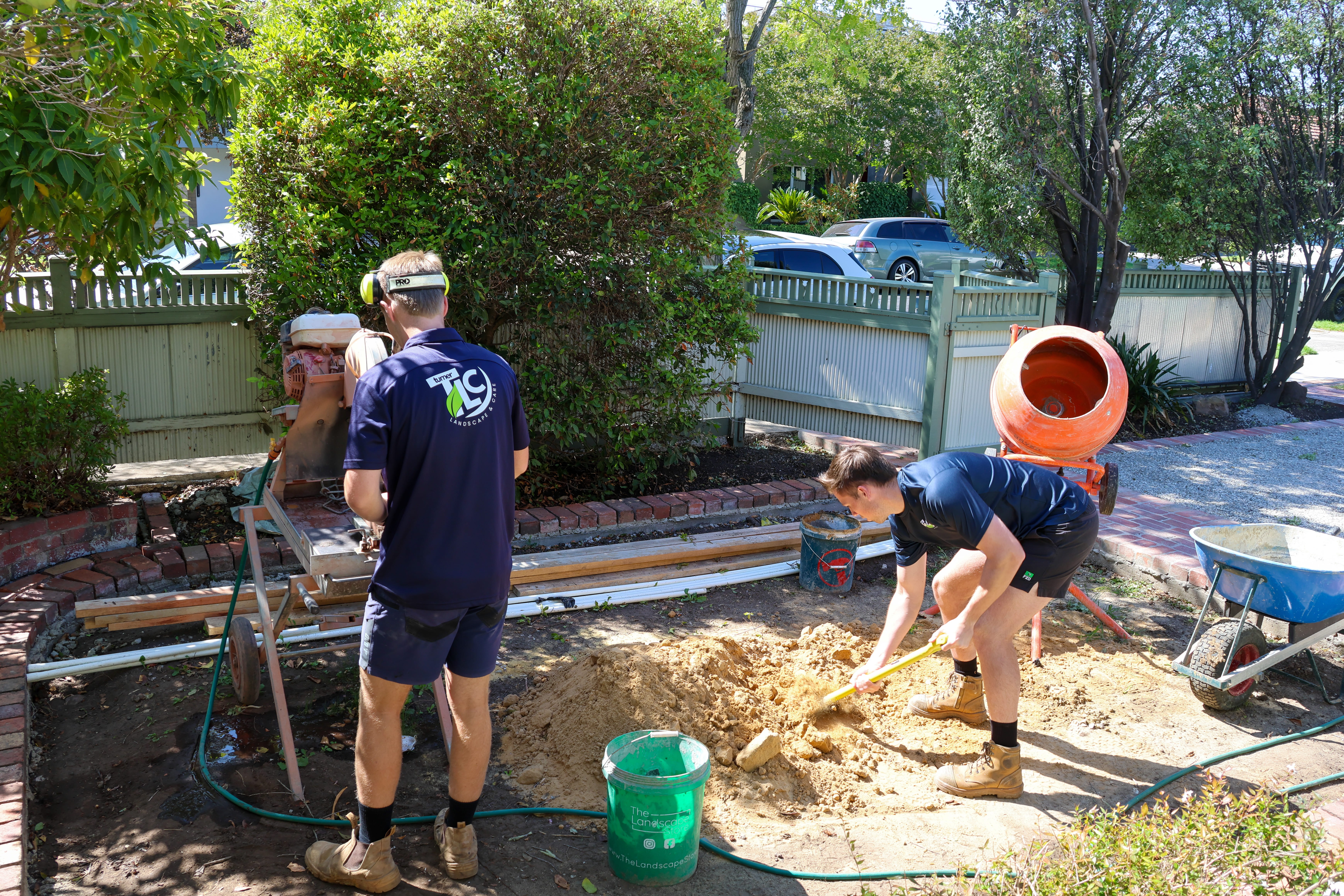 Two workers building a path with a saw, shovel, and cement mixer.