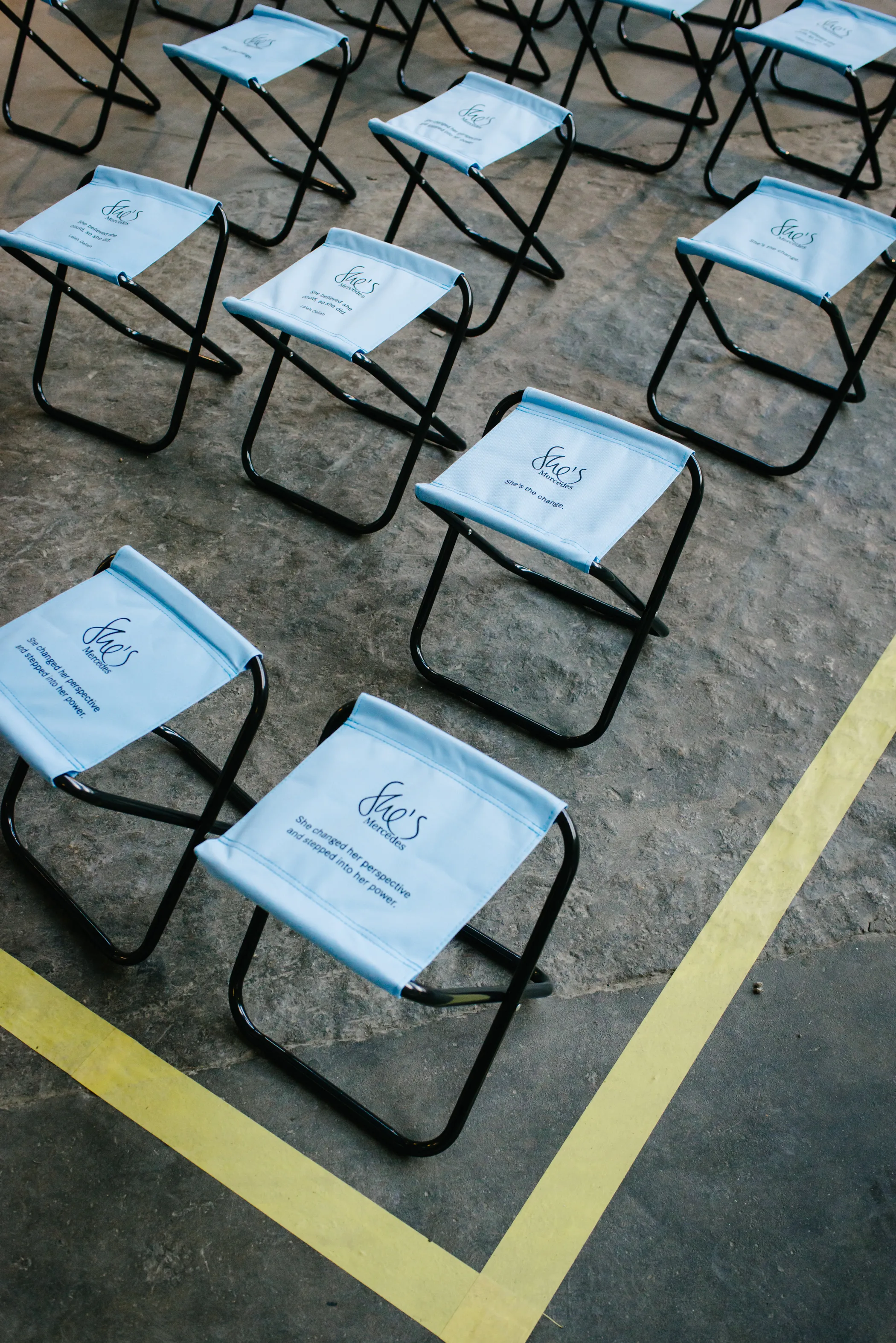 Rows of light blue branded folding stools on a concrete floor with yellow tape markings at the FEMALE FUTURE FORCE DAY.