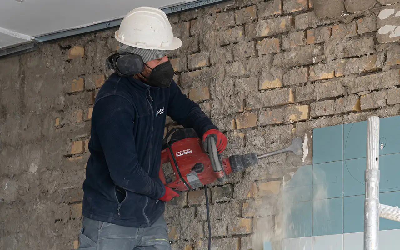 Arbeiter mit Bohrhammer bei Entkernungsarbeiten an einer Ziegelwand im Innenbereich