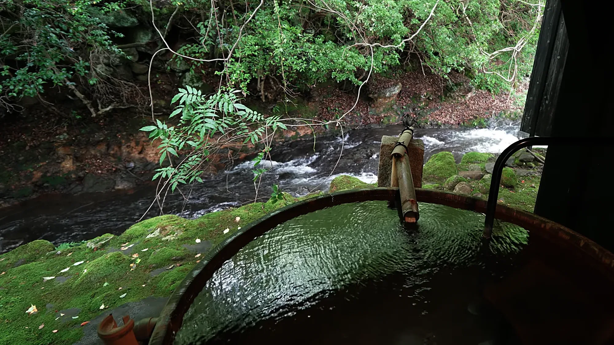 A timber tub at Kurokawa Onsen fed by a bamboo spout, a stream running behind