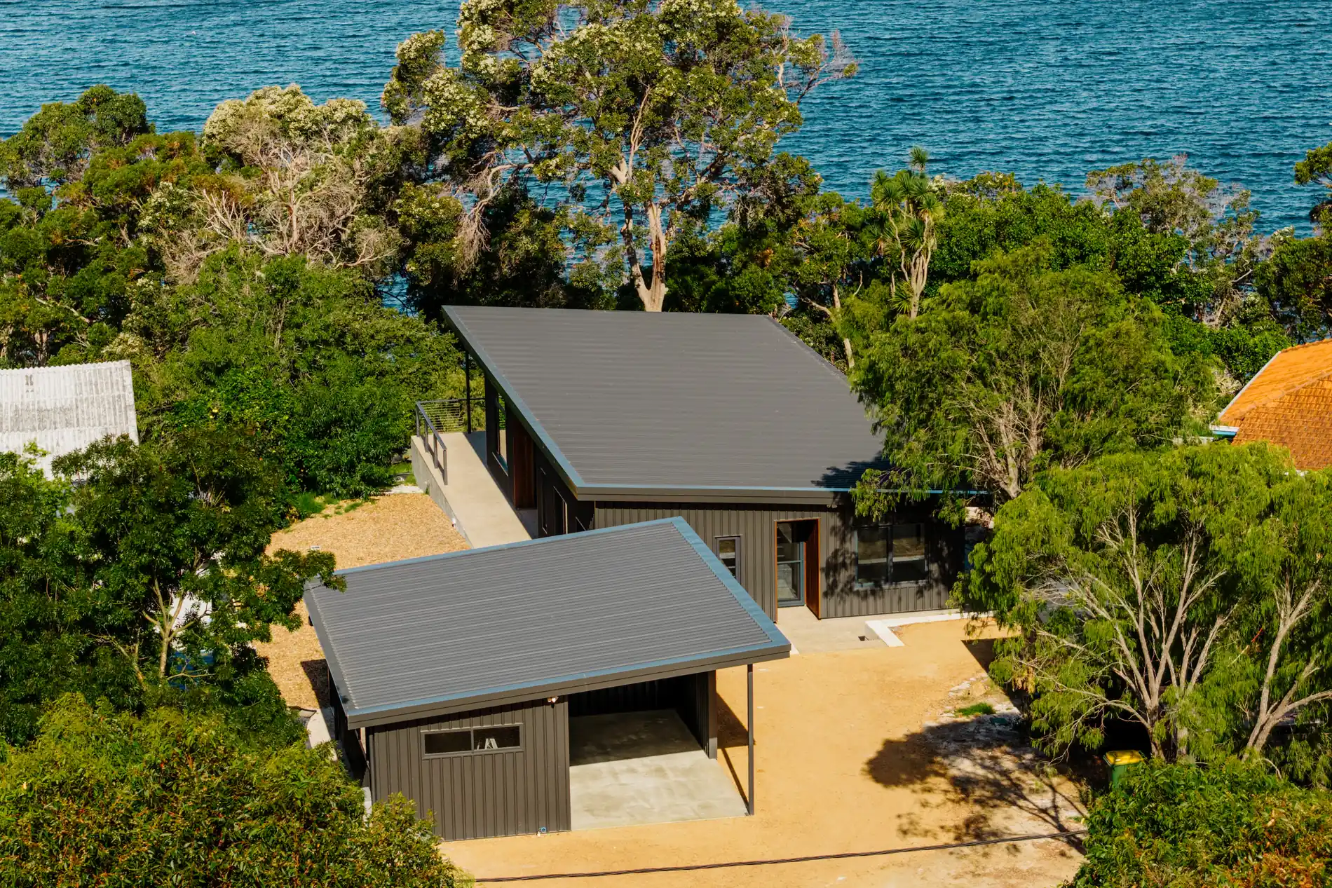 Aerial view of a finished dark-clad house among trees on the water's edge