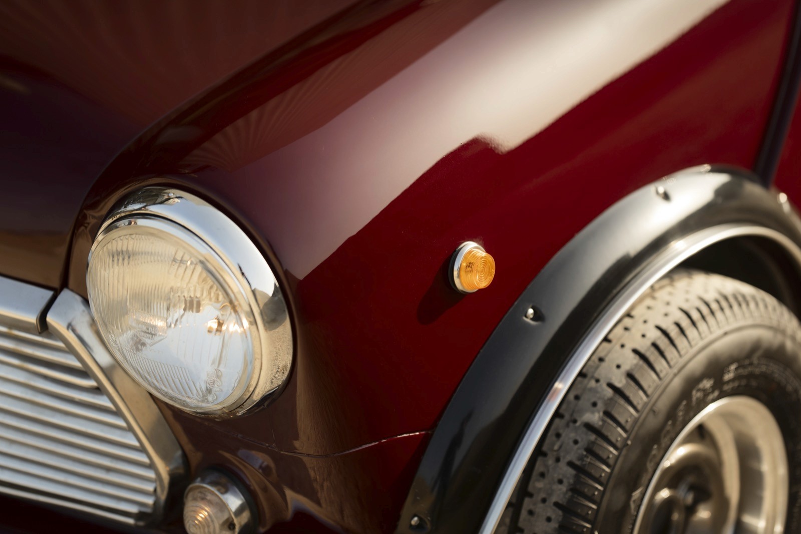 Close-up of a classic car's fender and headlight, featuring a shiny red finish and an elegant design.