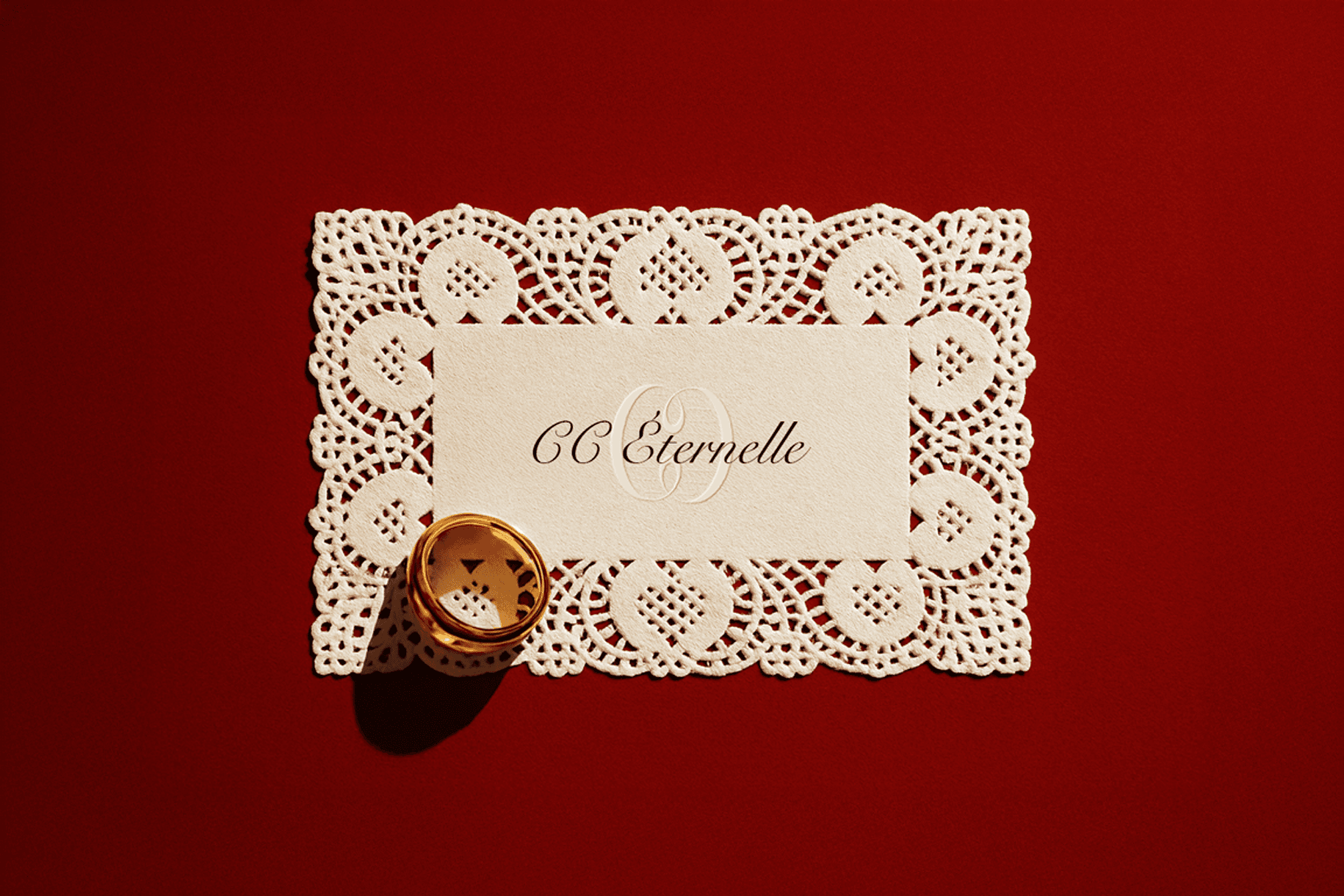 Decorative lace-edged card reading "CC Eternelle" placed on a red background with a gold ring resting on the corner.