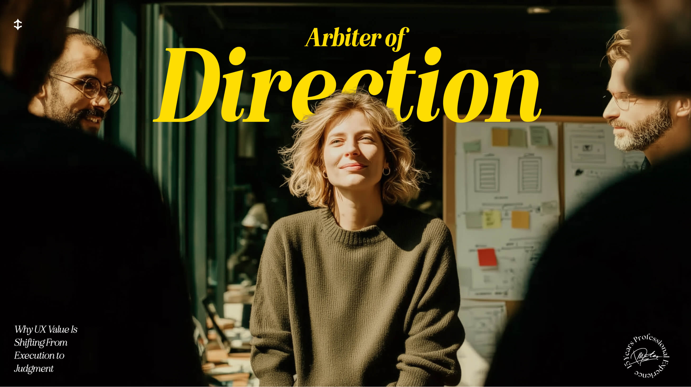 A UX designer standing in a collaborative studio space, facing a small group during a design discussion, with wireframes and notes visible on a board behind her.