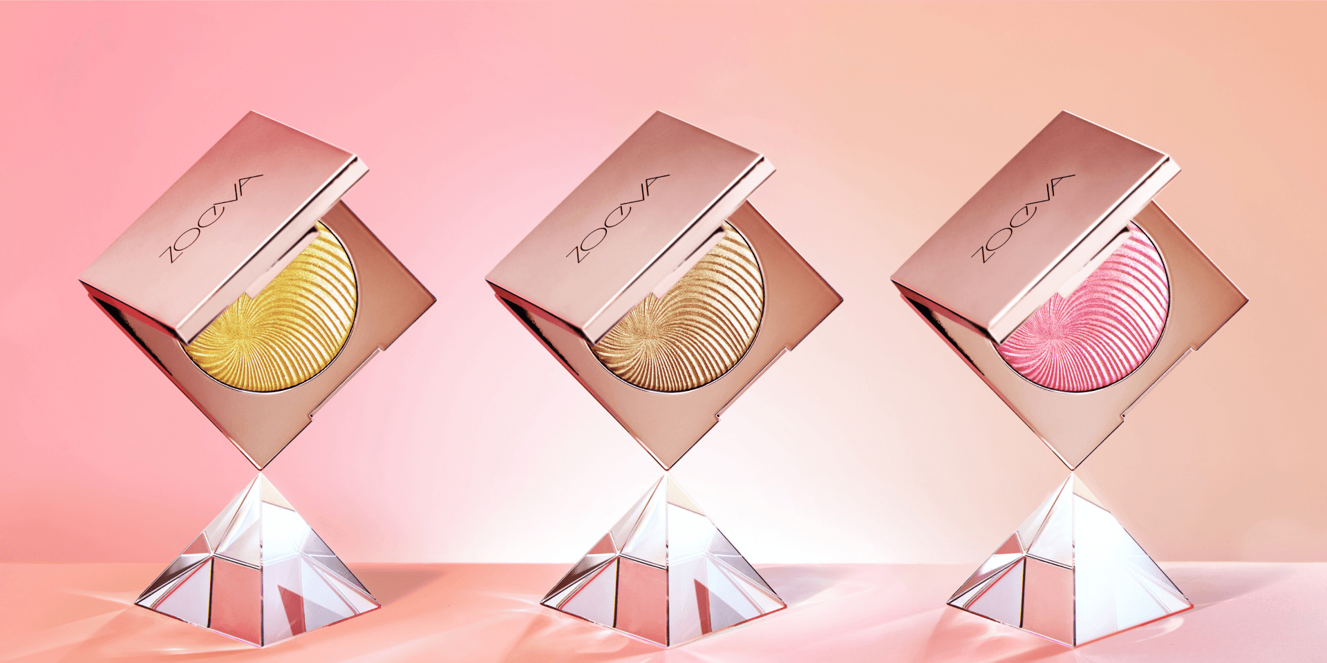 Markenwelt Zoeva – drei goldene Highlighter-Compacts auf Kristallsockeln vor zartrosa Hintergrund.