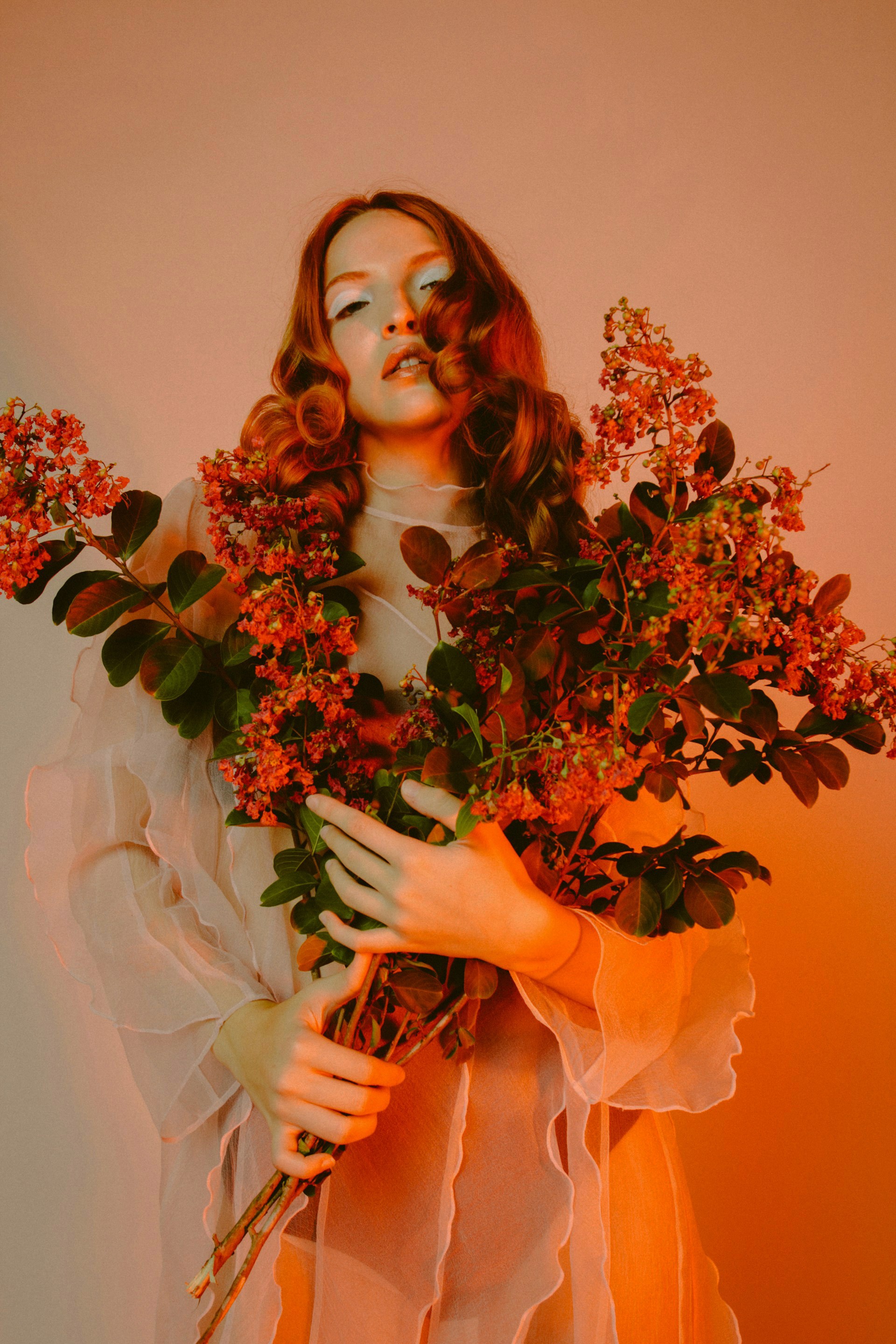 Woman with wavy hair holding a large bouquet of red flowering branches in warm light.