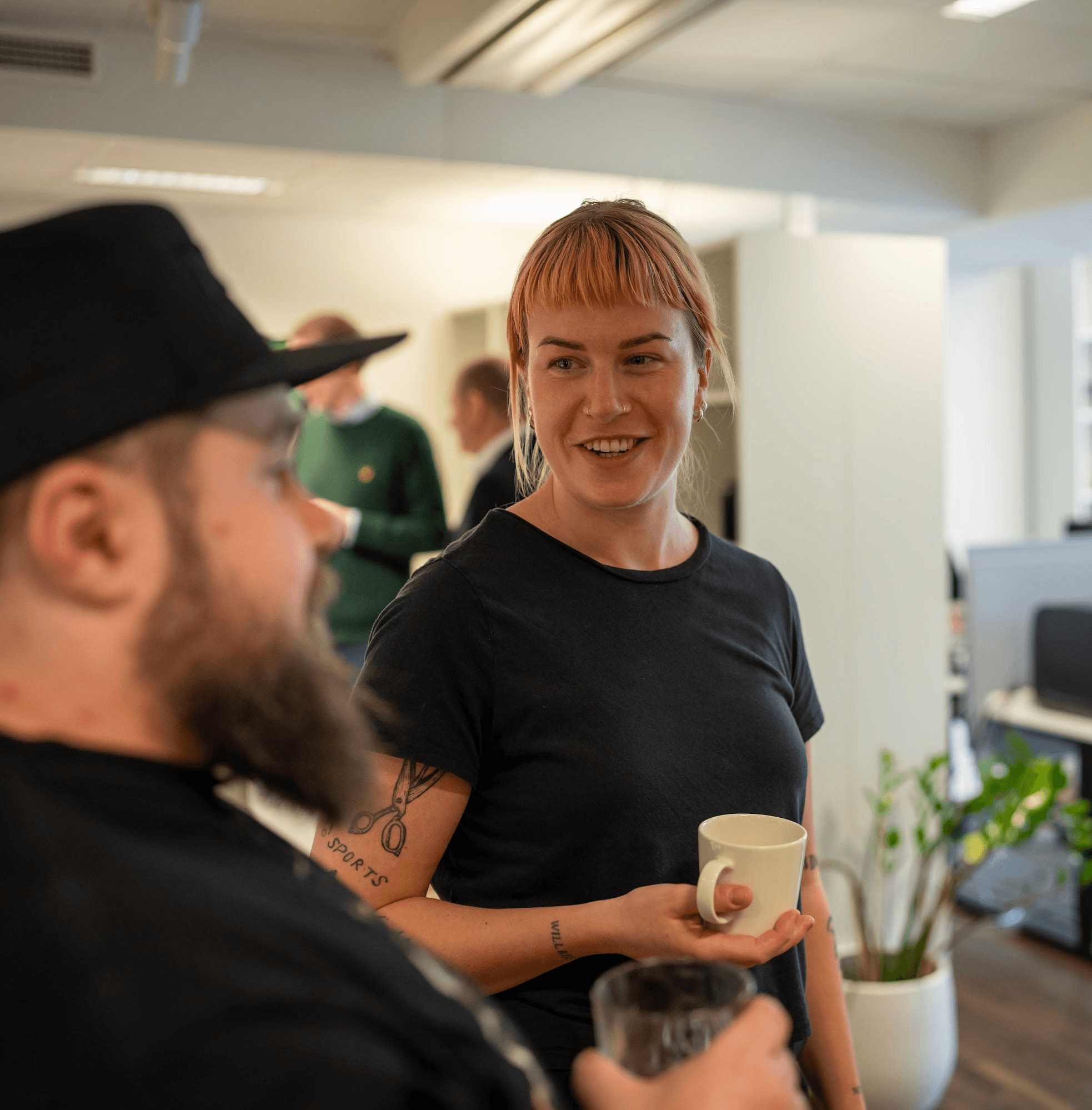 A smiling woman with her arms crossed, standing against a dark green background. She has long, dark hair.