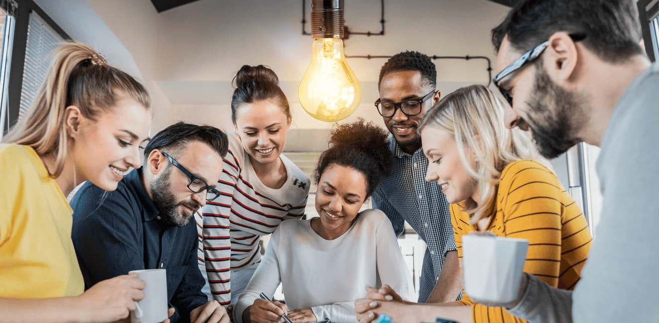 Diverse team collaborating around a table under a glowing lightbulb, illustrating innovative practices and shared problem-solving