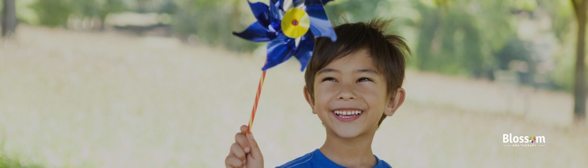 Child smiling while holding a colorful pinwheel in a park.