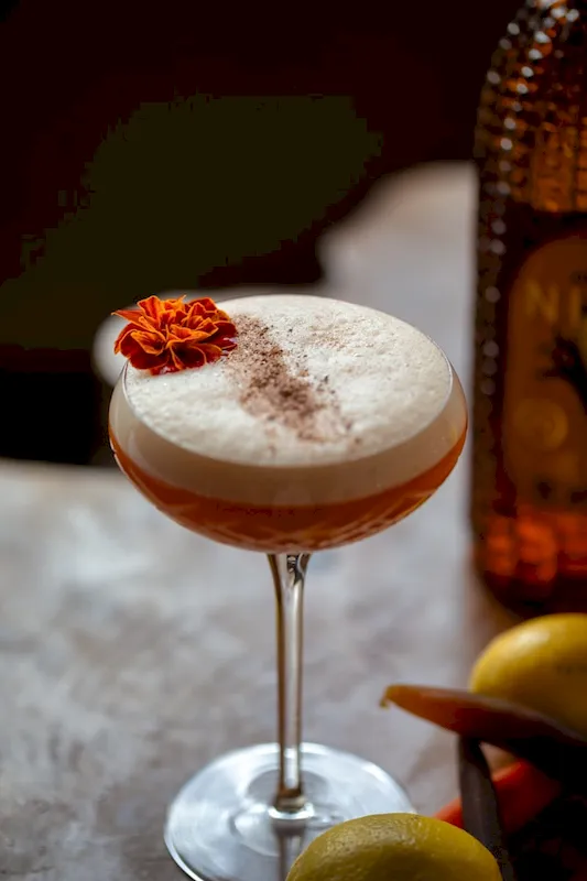 Pink egg white cocktail with an orange flower