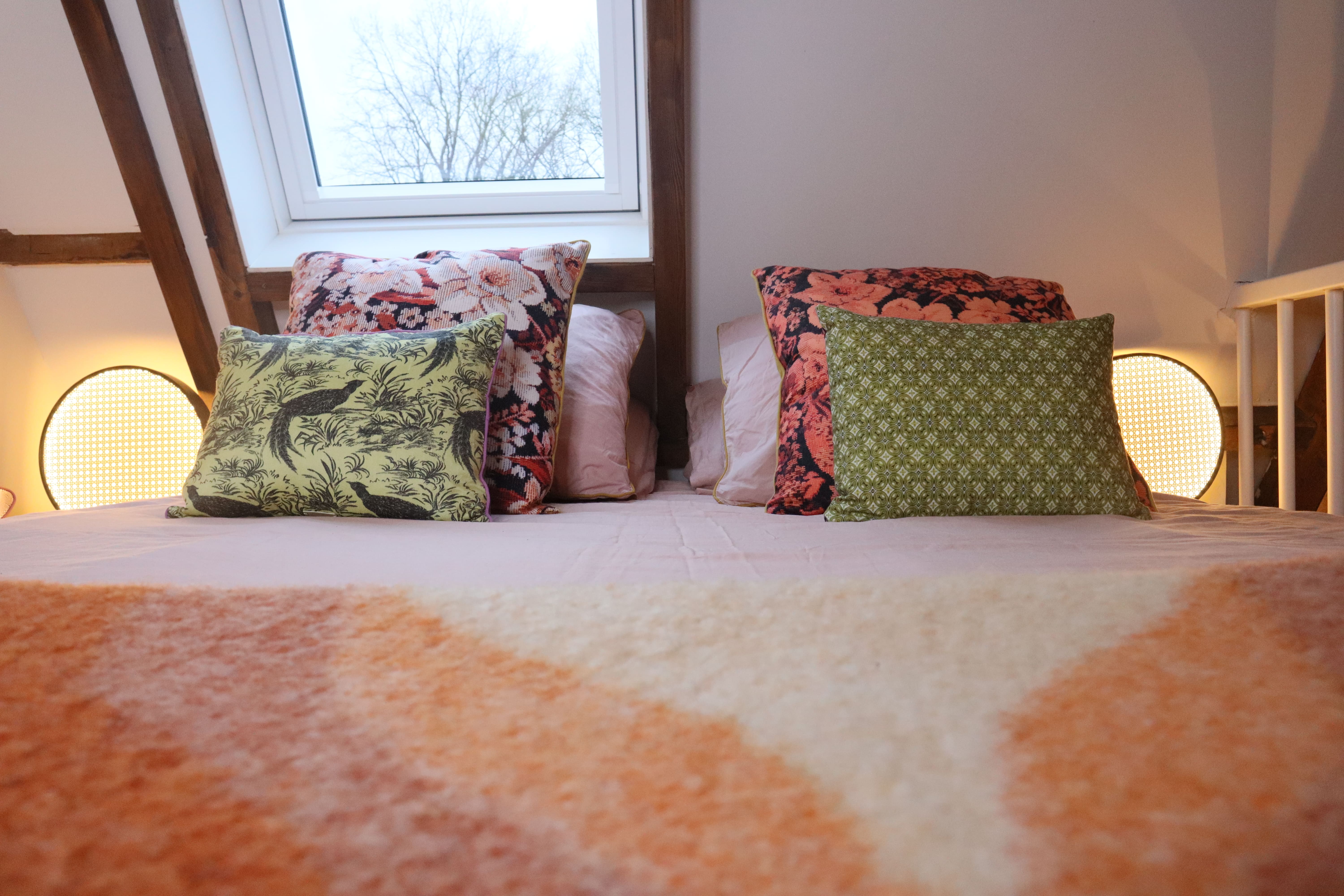 Slaapkamerhoek met een bed met kleurrijke kussens, een zacht beddengoed en een raam.
