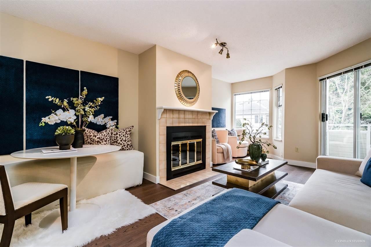 Cozy living room with a fireplace, modern decor, large windows, and a blue area rug on light carpet.