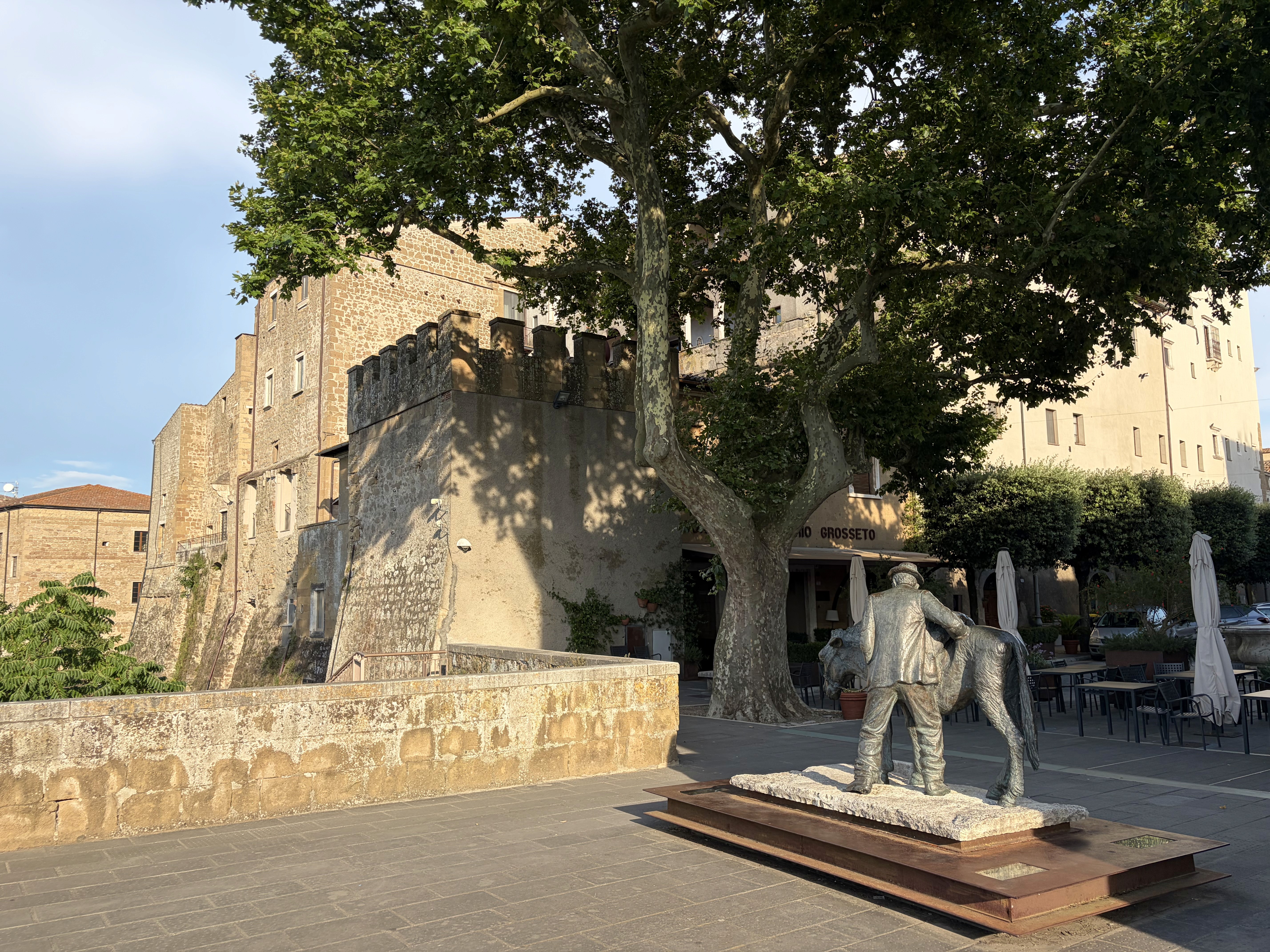 Piazza nel centro storico di Pitigliano, borgo della Maremma Toscana in provincia di Grosseto, con il bastione medievale e la statua in bronzo del contadino con l'asino