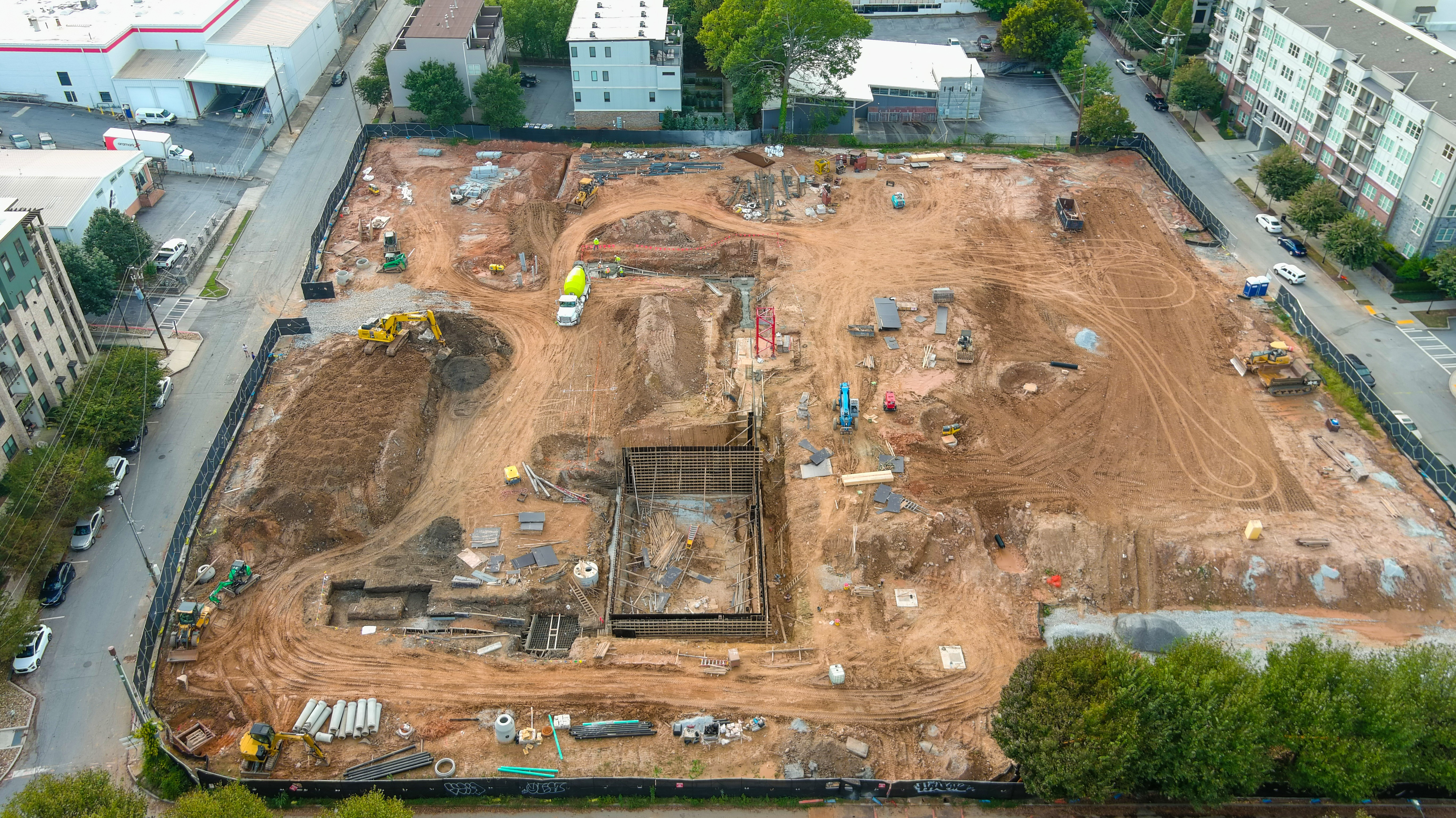 Aerial view of a large, cleared construction site with dirt, machinery, and some greenery surrounding the area.