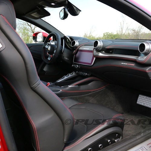 Interior of a modern sports car with black seats, red stitching, a touchscreen dashboard, and a steering wheel with controls.