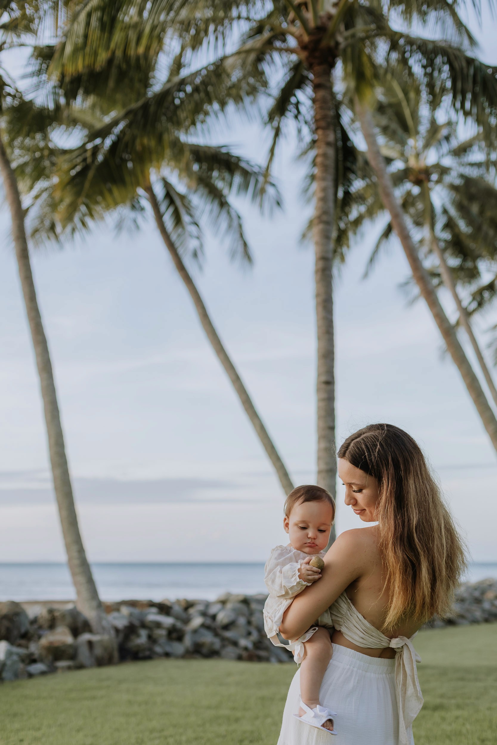 Mother and daughter cuddling together in tropical palm tree area during a lifestyle motherhood photoshoot