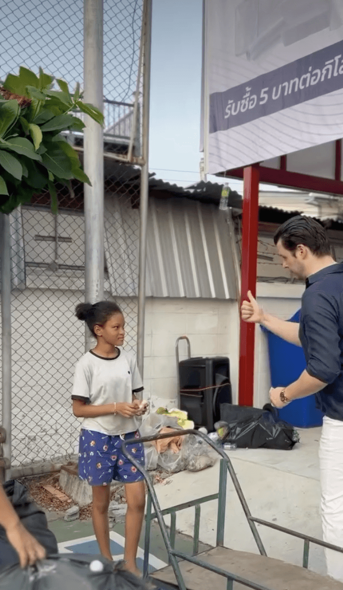 man in blue t-shirt and white floral skirt holding black smartphone while sitting on sidewalk